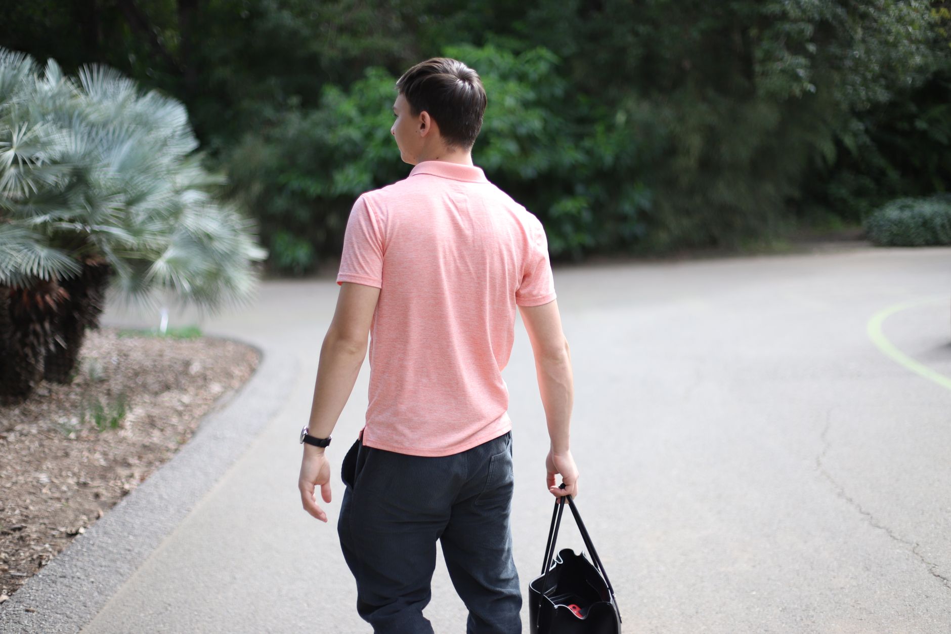 Man in a pink polo shirt walking outdoors with a tote bag, embracing a relaxed lifestyle.
