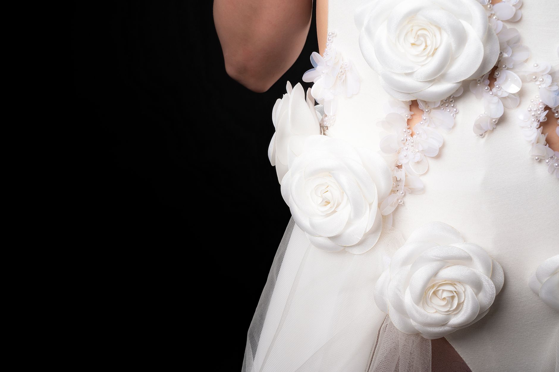 Close-up of a white dress adorned with large floral appliques on a black background.