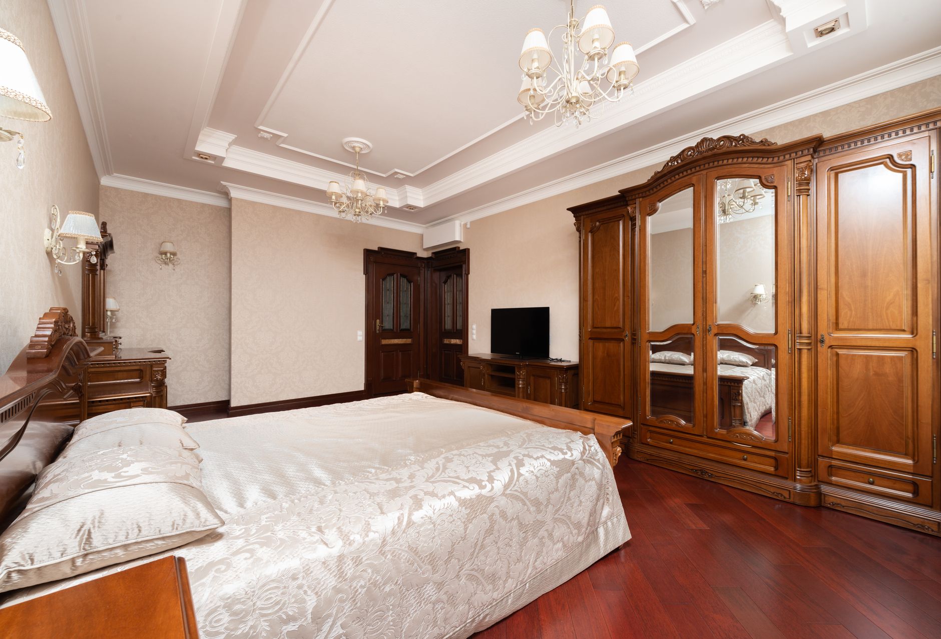 Luxurious bedroom with wooden furniture, chandeliers, and lavish bed linens creating a warm ambiance.