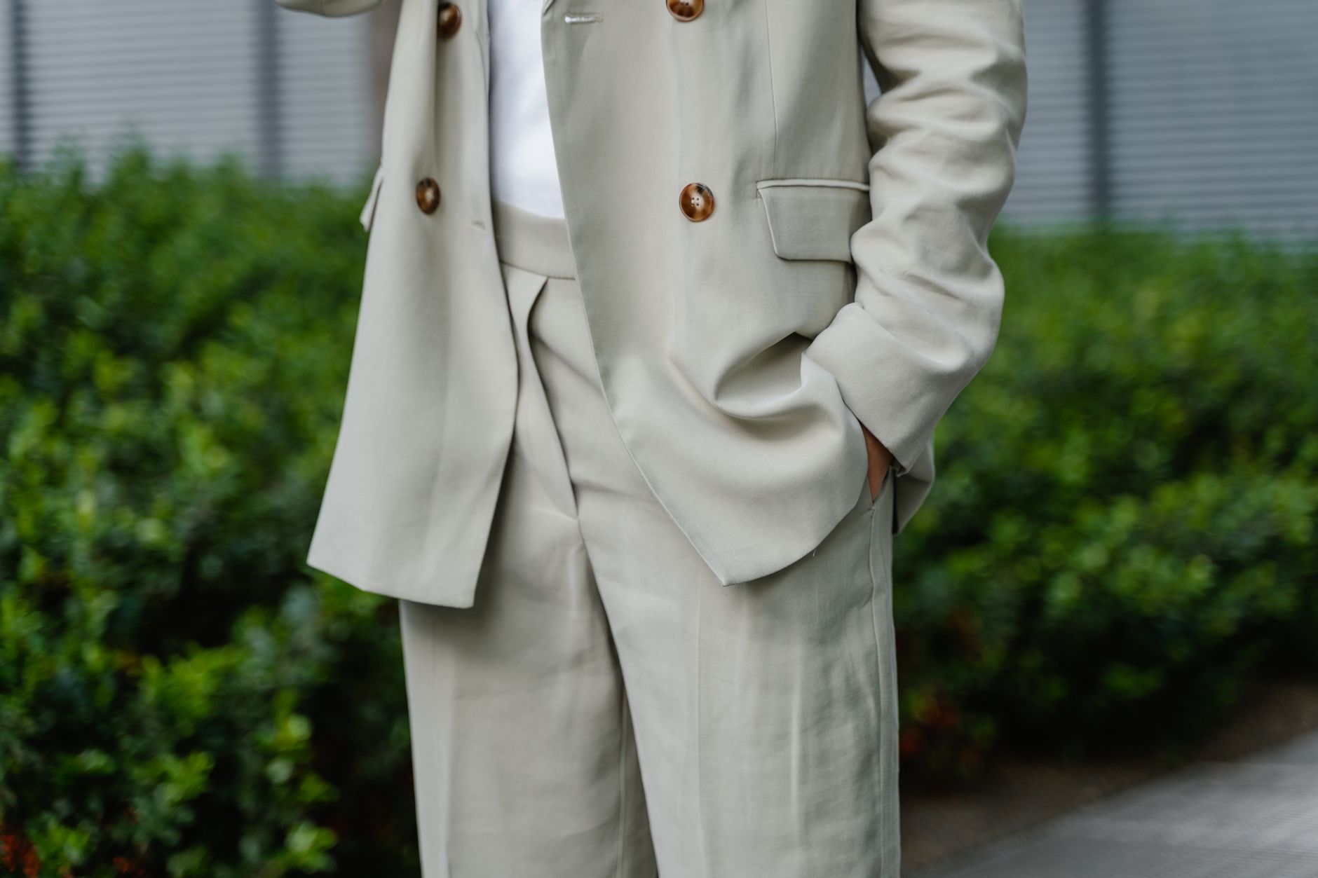 Close-up of an unrecognizable person wearing a stylish beige suit with hands in pockets outdoors.