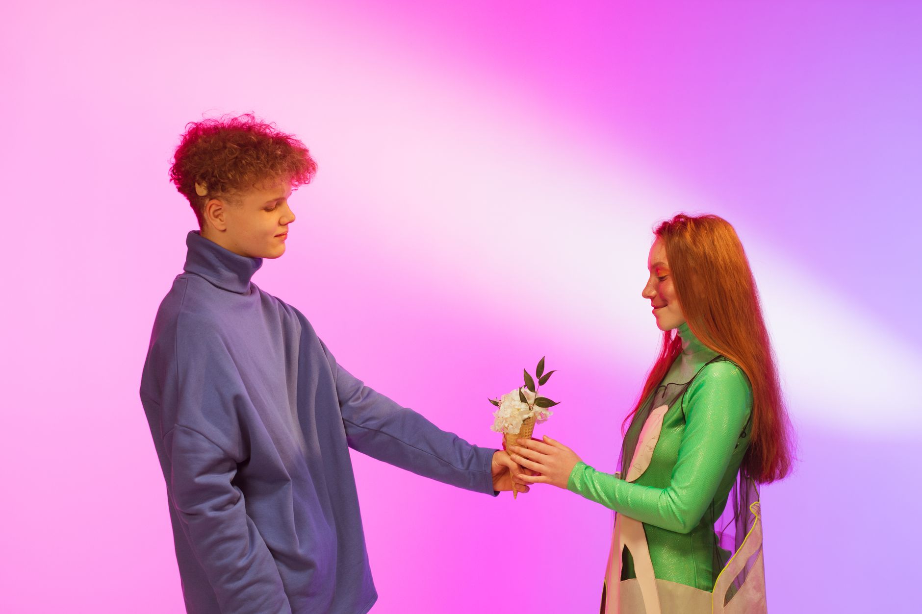 A young couple in a studio exchanging flowers on a colorful background.