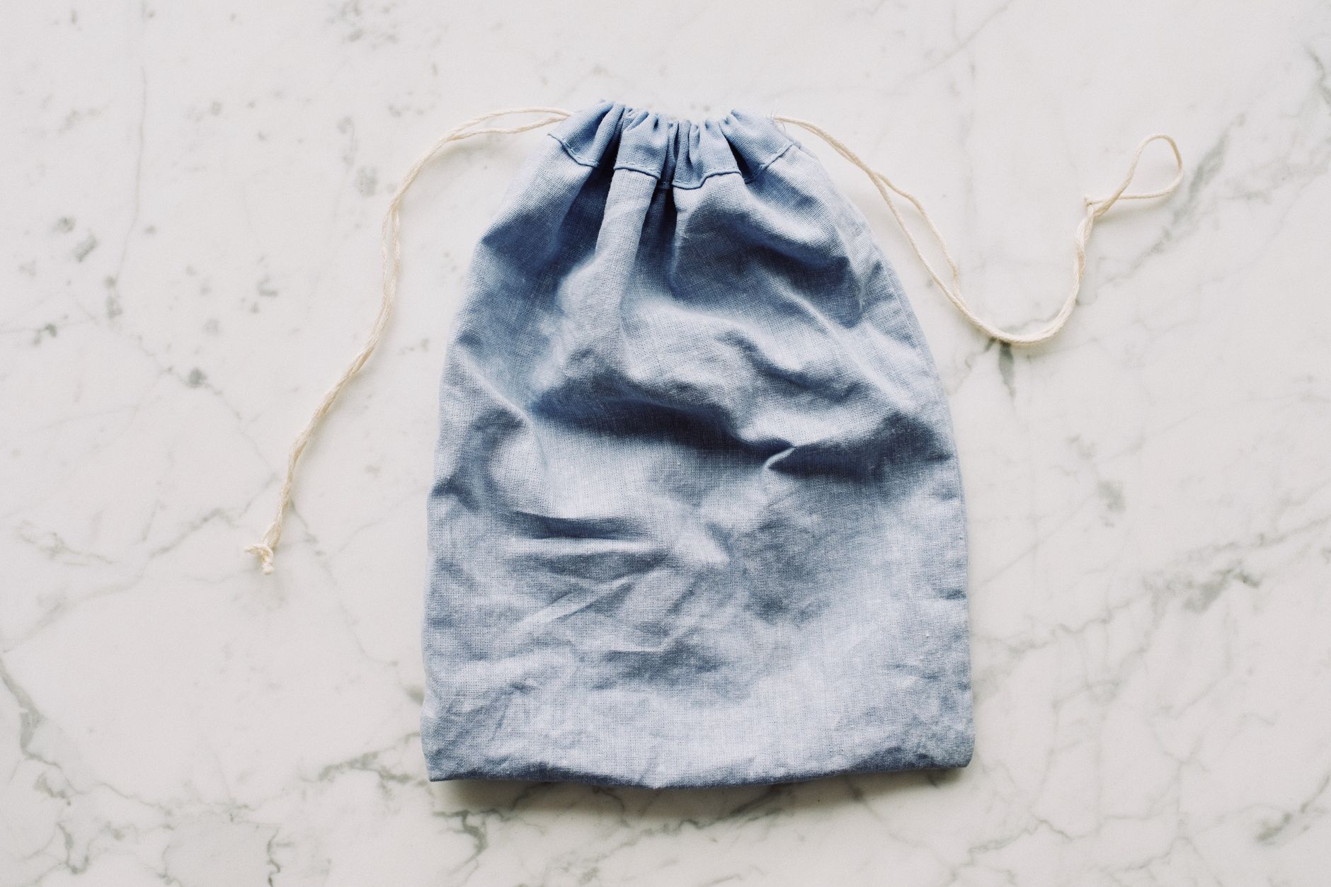 Top view of blue empty fabric reusable bag with white drawstrings placed on marble surface in light room