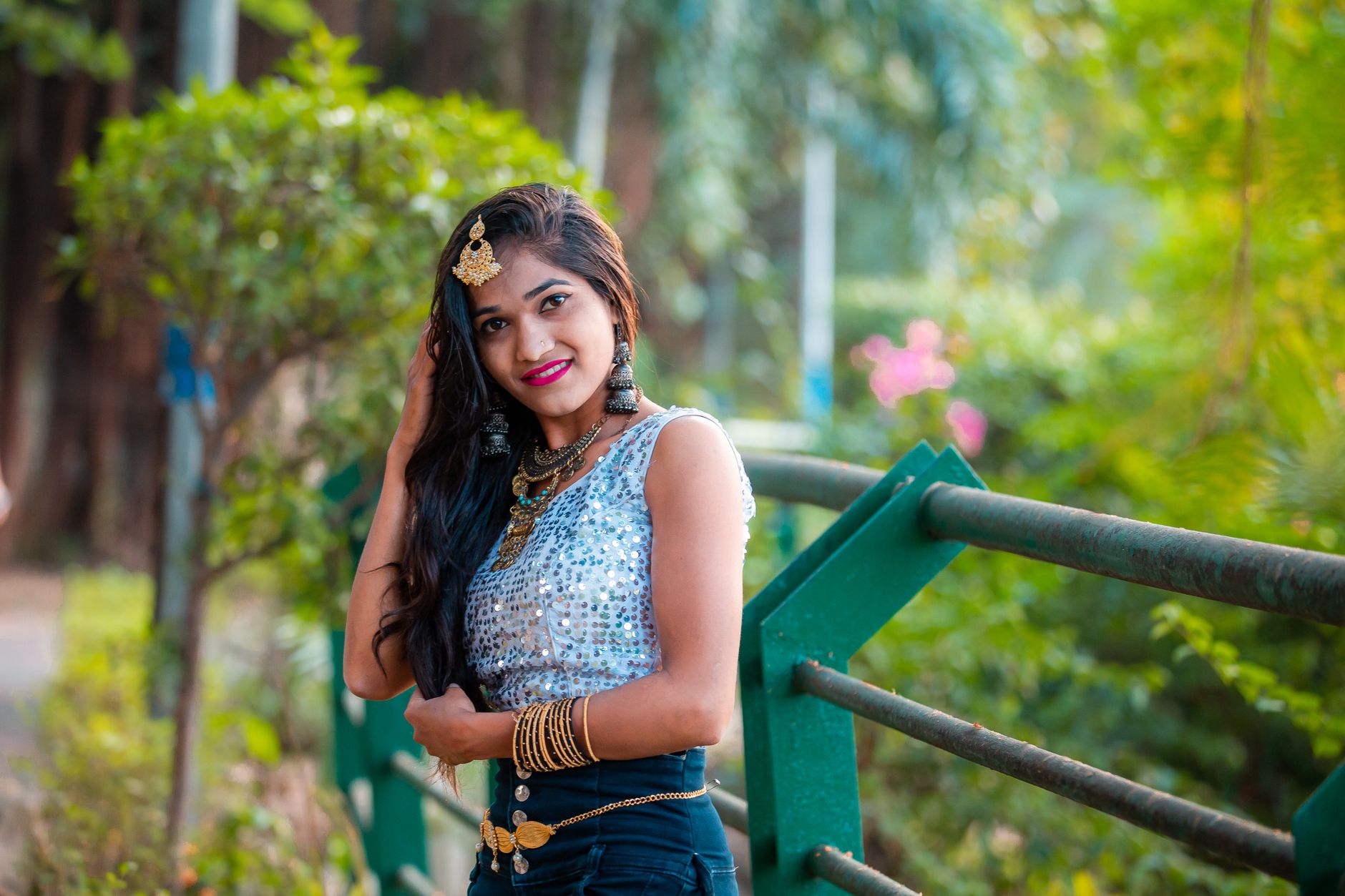 Young woman in a sequined top posing in a park setting, showcasing fashion and style.