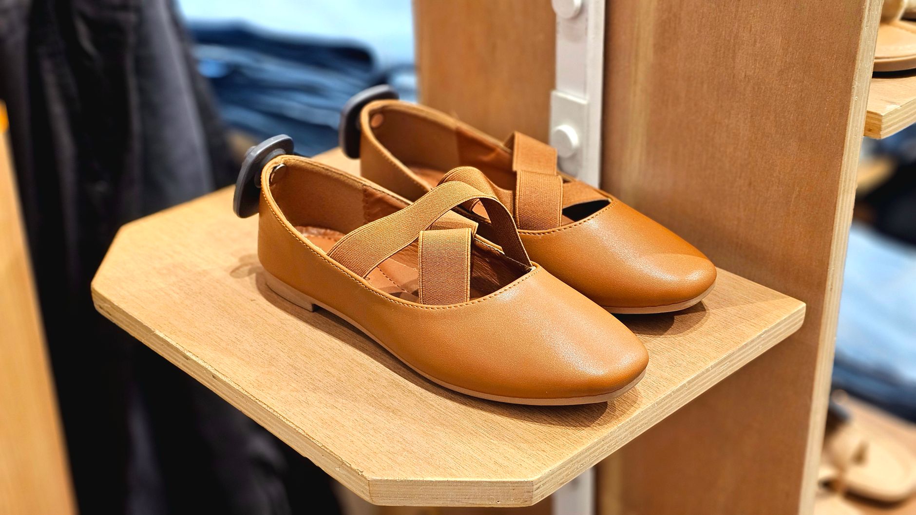 Pair of brown leather ballet flats with cross straps, showcased on a wooden shelf.