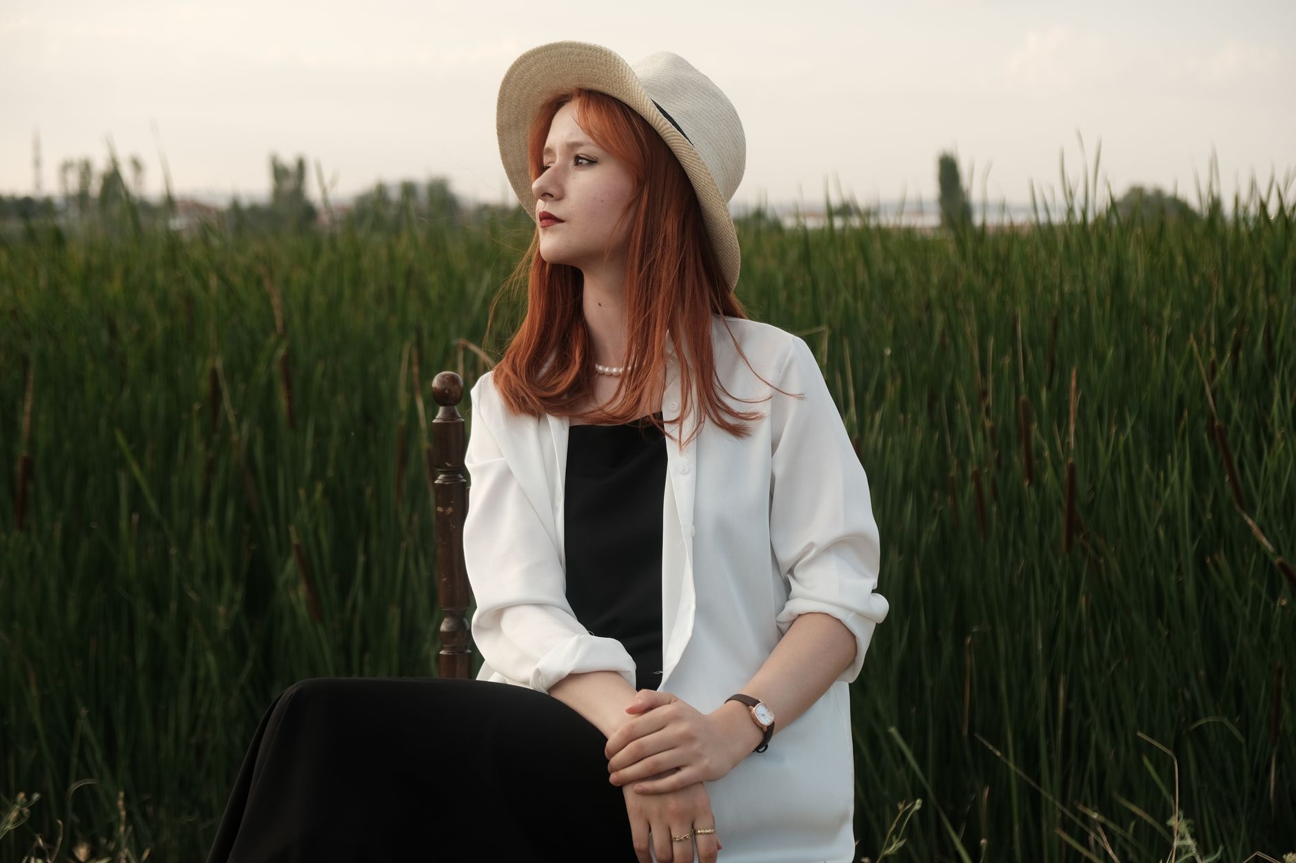 Portrait of a stylish woman in a hat sitting in a grassy field during summer.