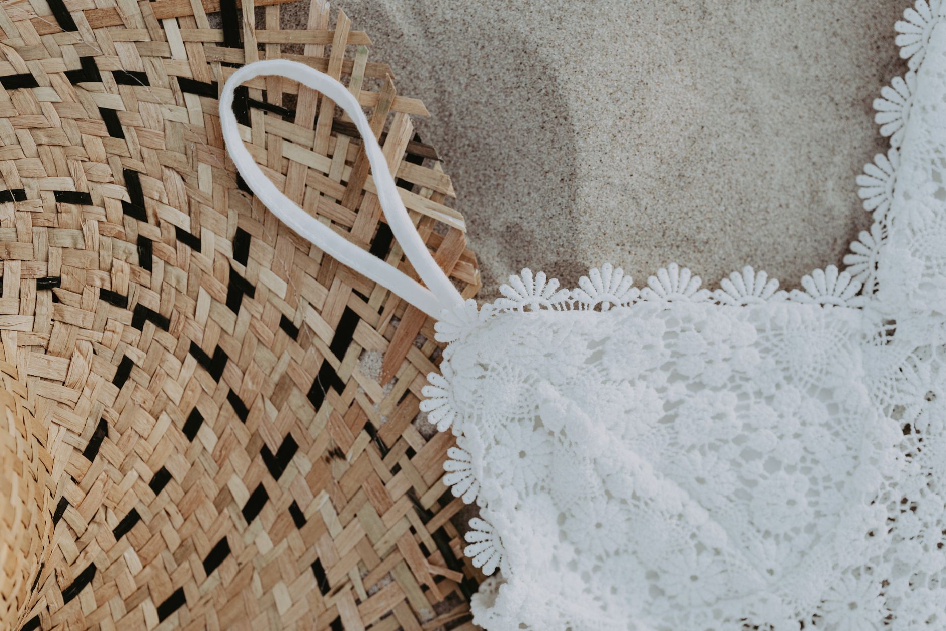 Close-up of a lace swimsuit and straw hat on sand, evoking a summer beach vibe.