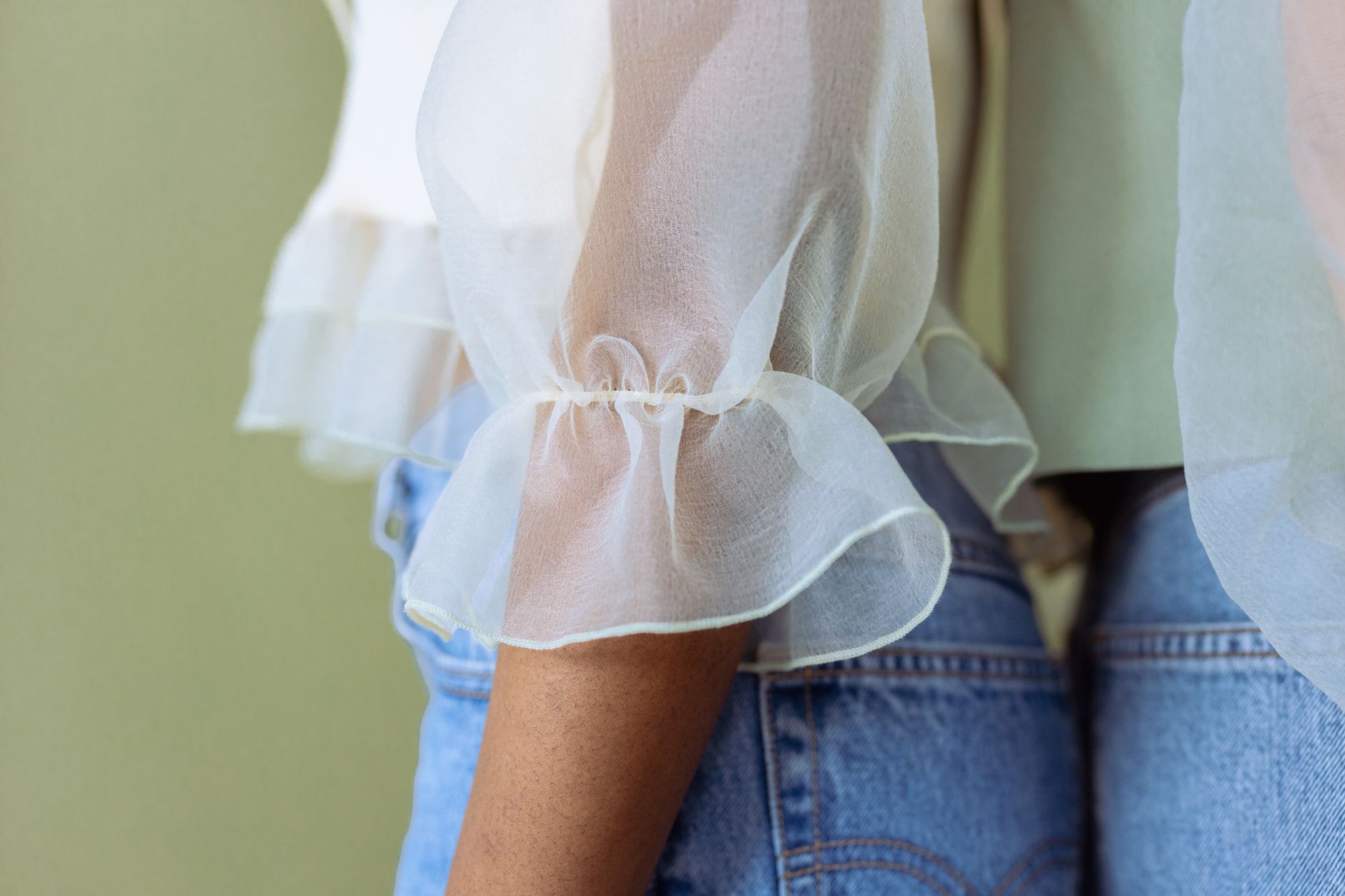 Close-up of a sheer white blouse with ruffles paired with denim jeans, showcasing modern fashion.