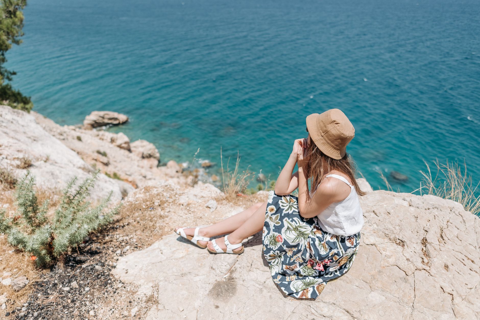 A woman in a floral skirt and hat enjoys a coastal view, perfect for travel and lifestyle themes.