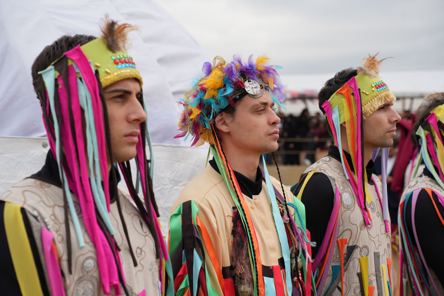 Participants in vibrant traditional costumes showcase colorful headgear at an outdoor festival parade.