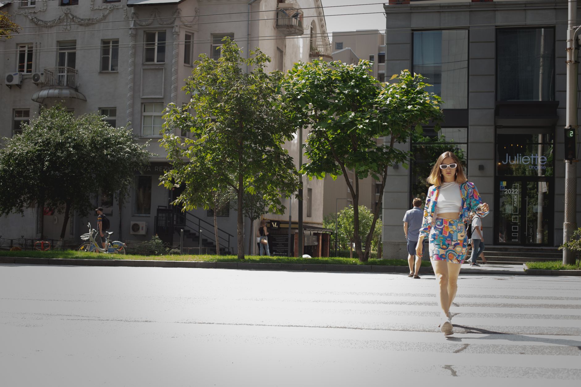 A fashionable woman crosses a city street in bright urban attire, exuding confidence and style.