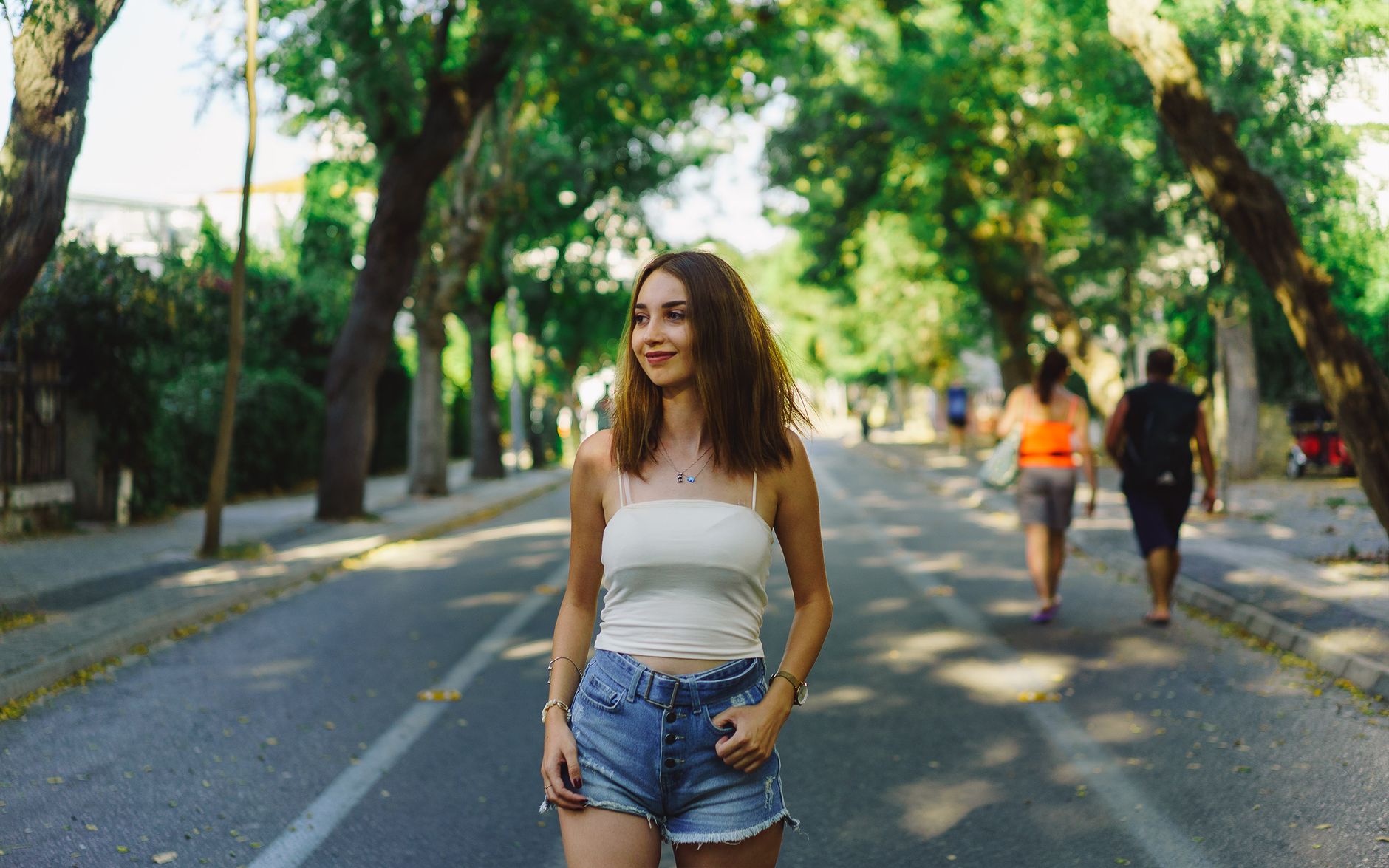 Smiling woman in casual attire taking a stroll on a sunny park road.