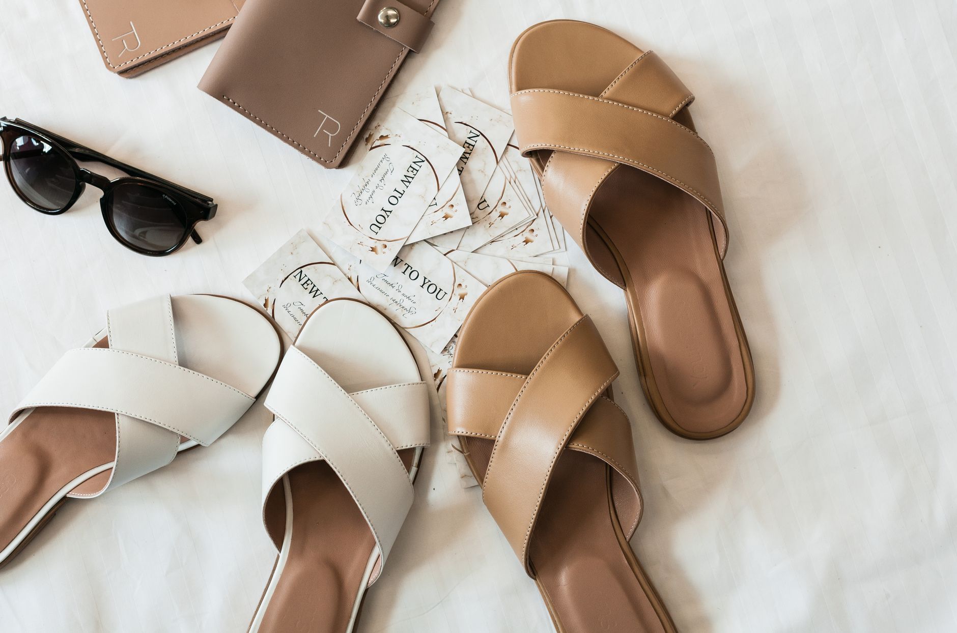 Flat lay of elegant leather sandals, sunglasses, and wallet on a neutral background.