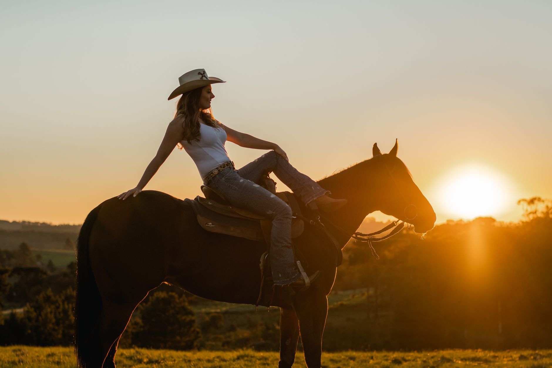 A serene silhouette of a woman in a cowboy hat riding a horse at sunset in a field.
