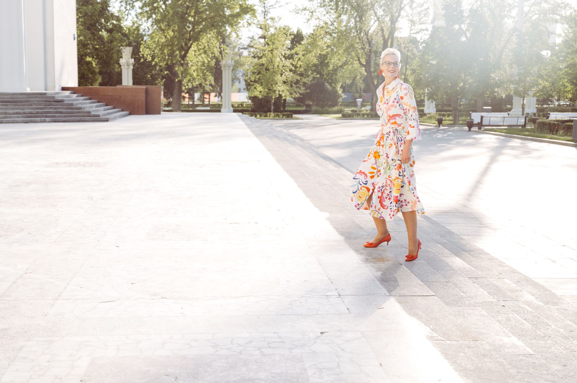 A fashionable senior woman in a vibrant dress walking outdoors on a sunny day.