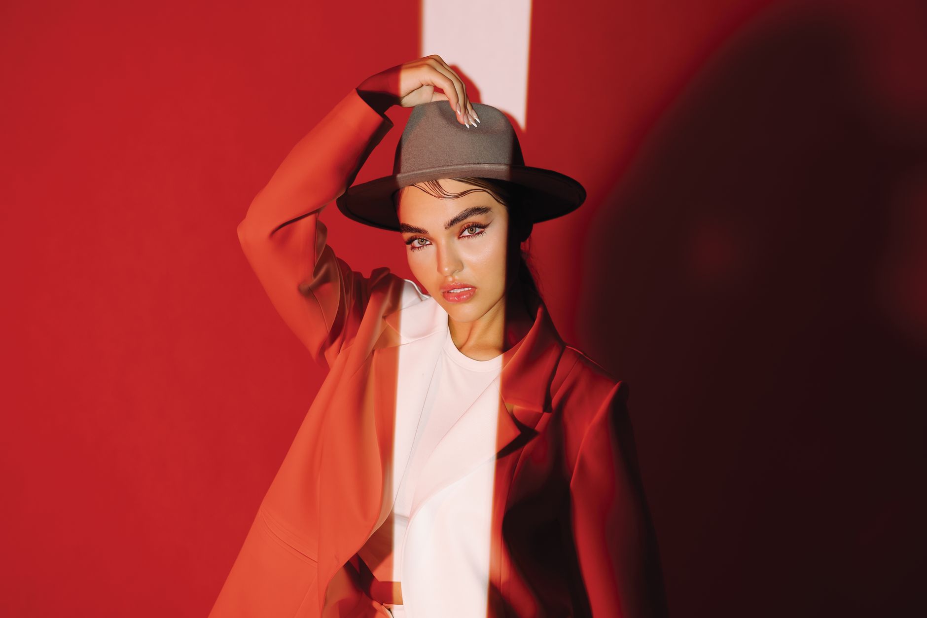 Fashion portrait of a woman in a red suit and hat striking a pose against a vibrant backdrop.