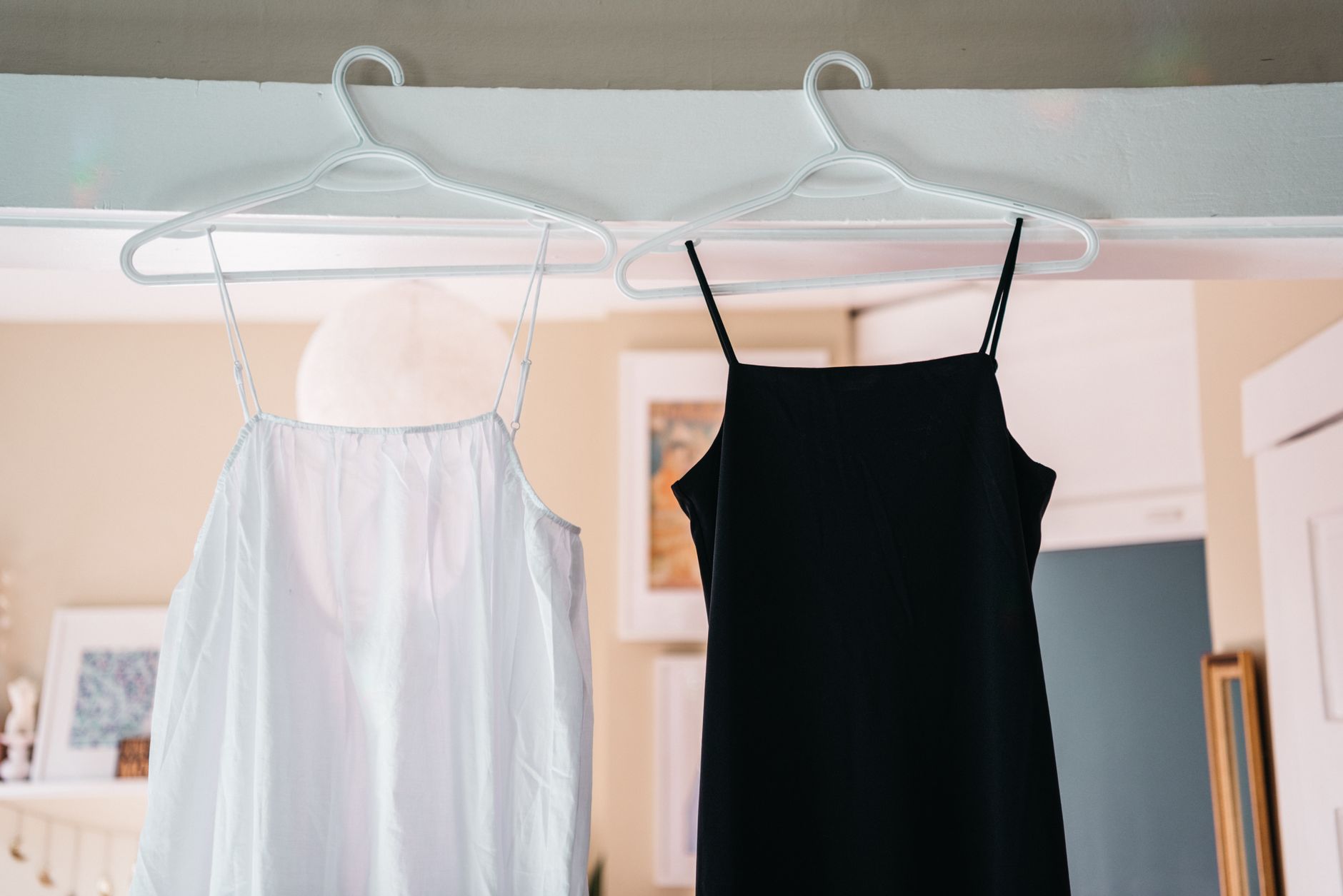 Minimalist display of black and white spaghetti strap dresses hanging indoors.