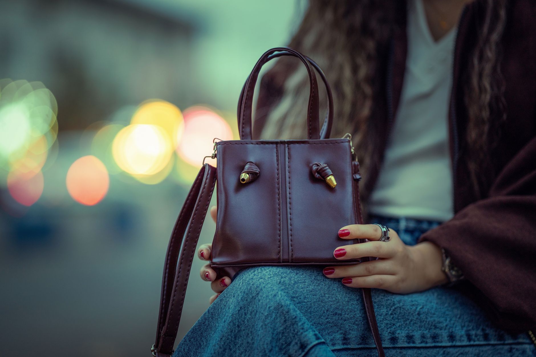 Trendy brown leather handbag held by a woman with city lights as backdrop.