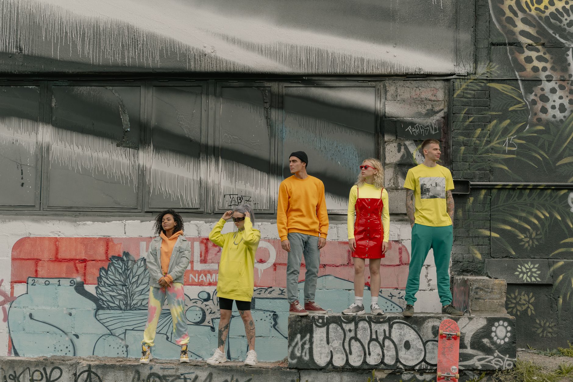 Fashionable group standing against vibrant graffiti wall, showcasing modern street style.