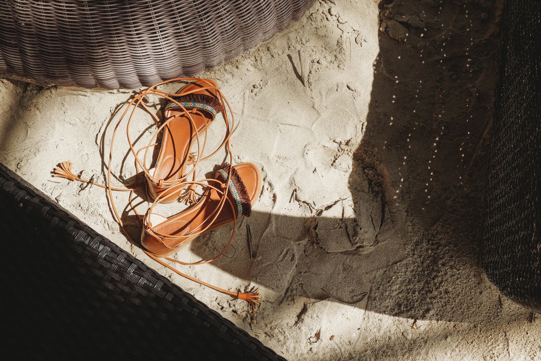 Close-up of brown sandals with tassels on beach sand, captured in sunlight. Perfect for summer vibes.