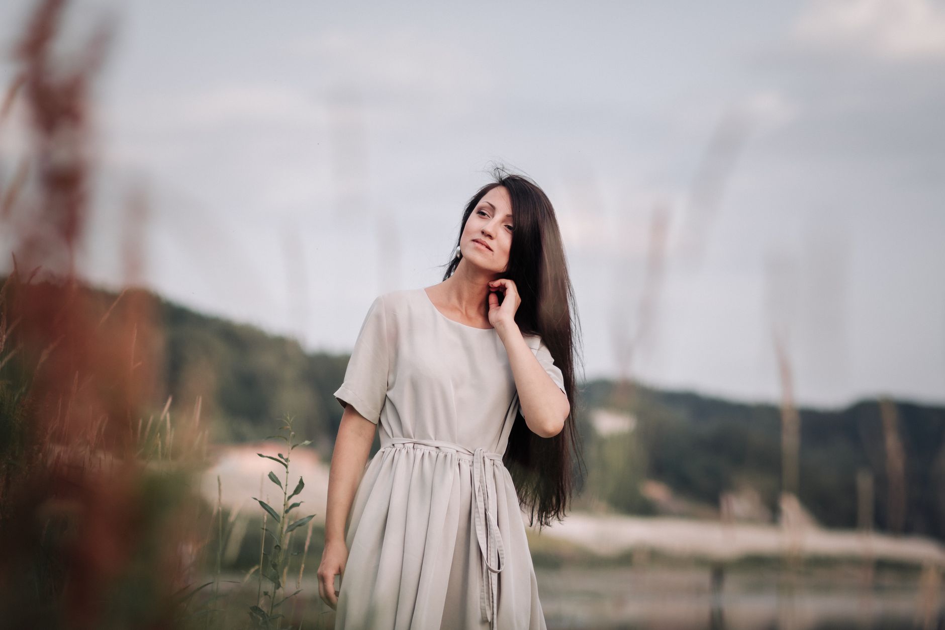 Woman in a grey dress posing outdoors amidst greenery with a serene look