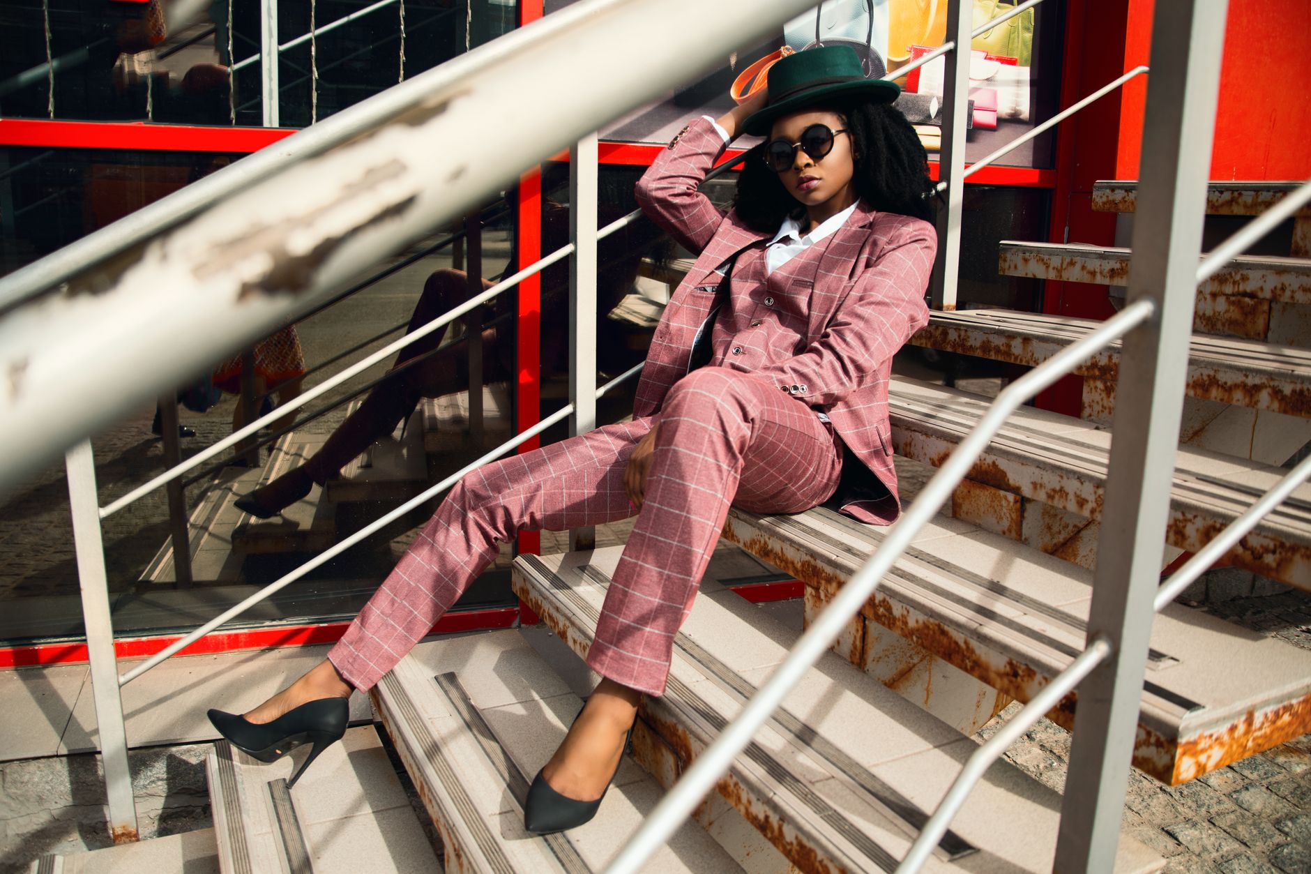 Fashionable woman in pink plaid suit and hat posing on an urban staircase.