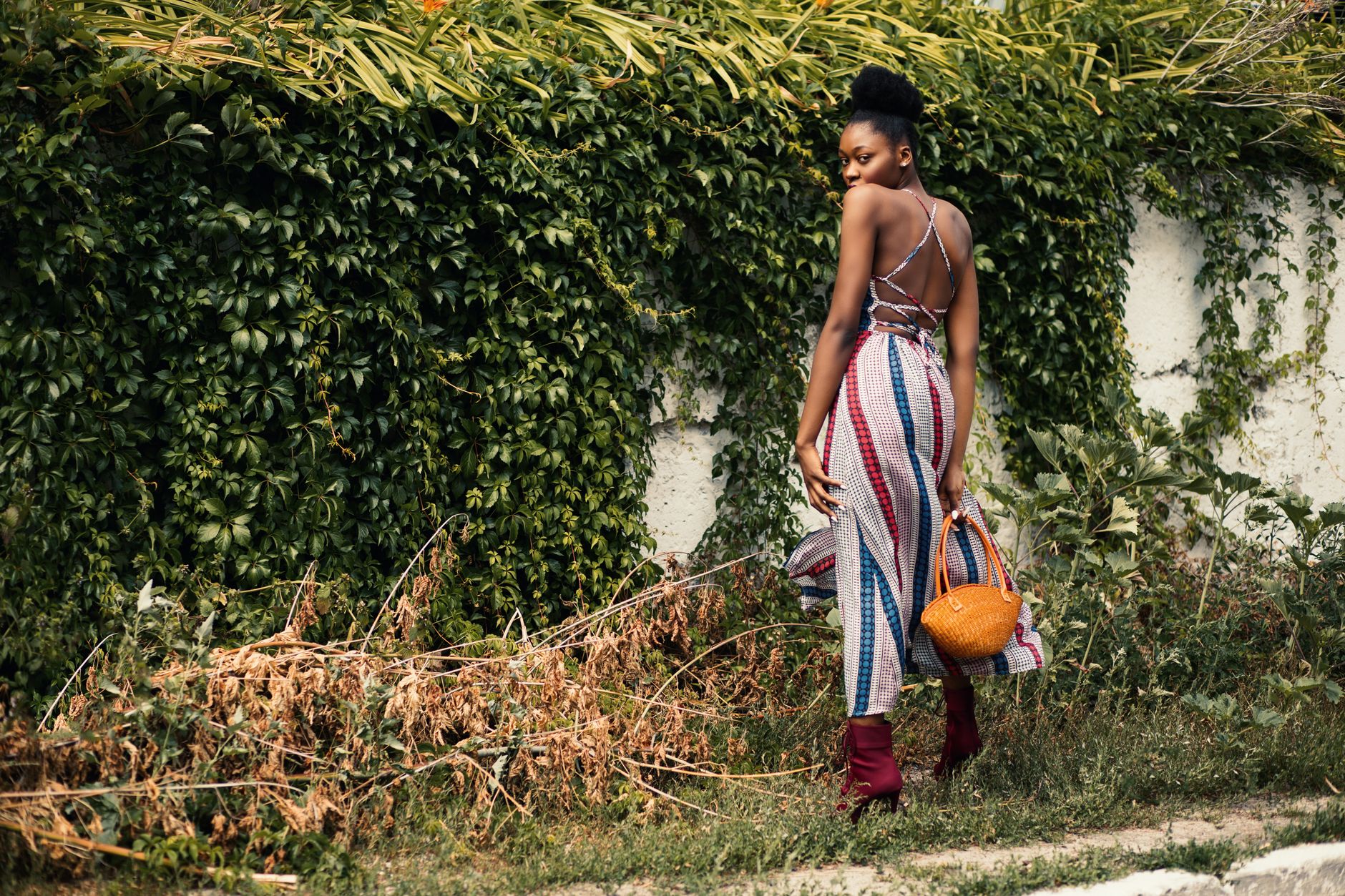 A fashionable woman poses in a vibrant summer dress against a lush green backdrop.