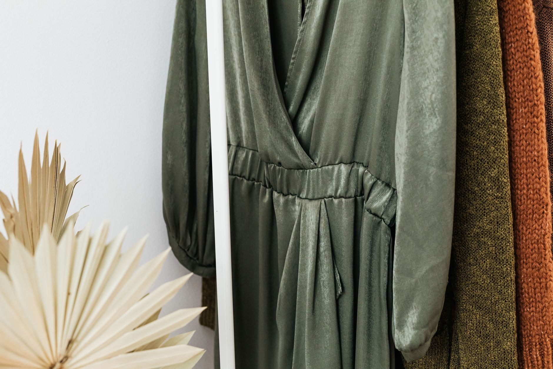 Stylish green dress on a clothes rack with knitted sweaters and dried leaves in a cozy setting.