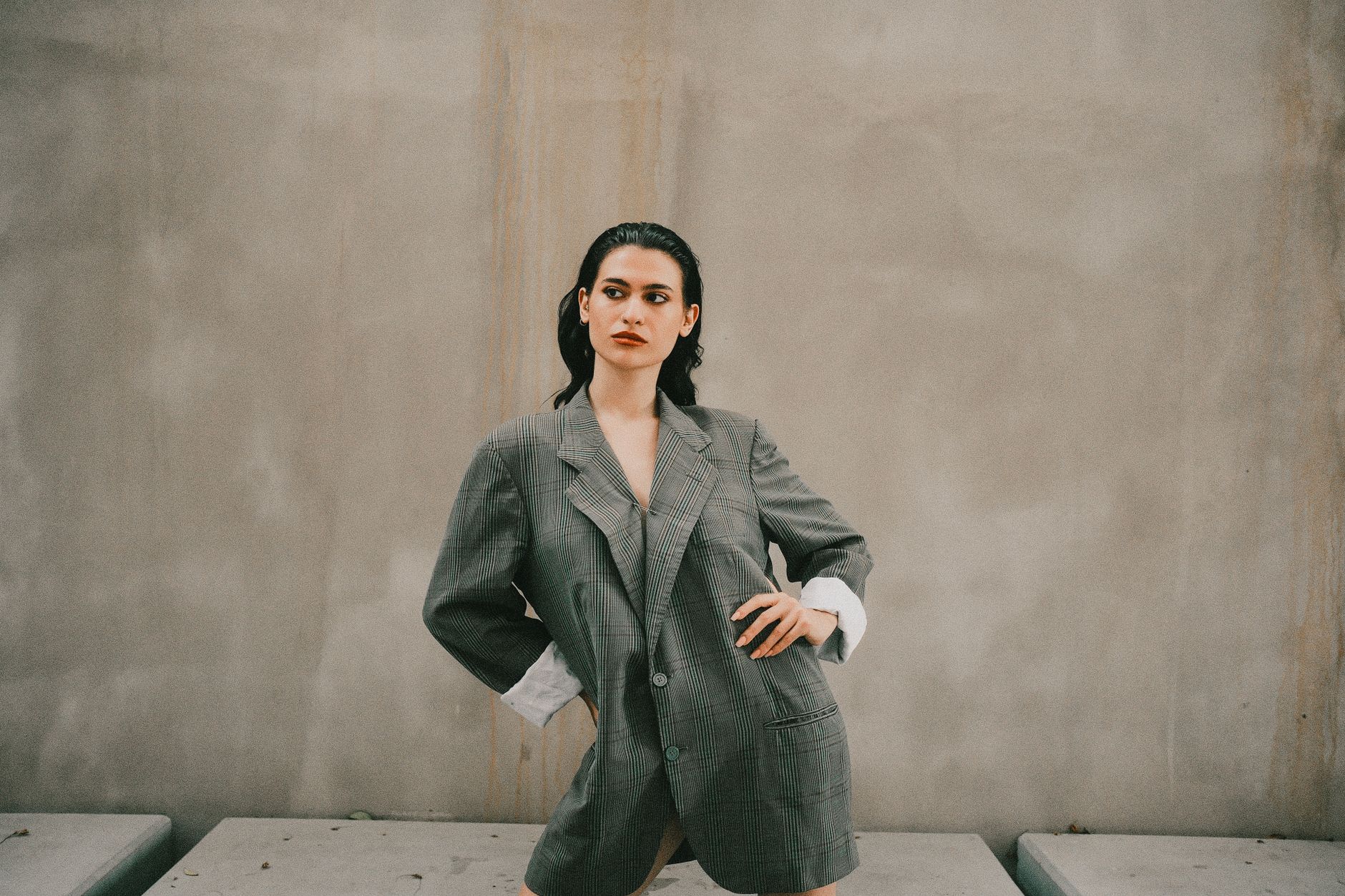 Stylish woman posing in oversized suit against minimalist backdrop.