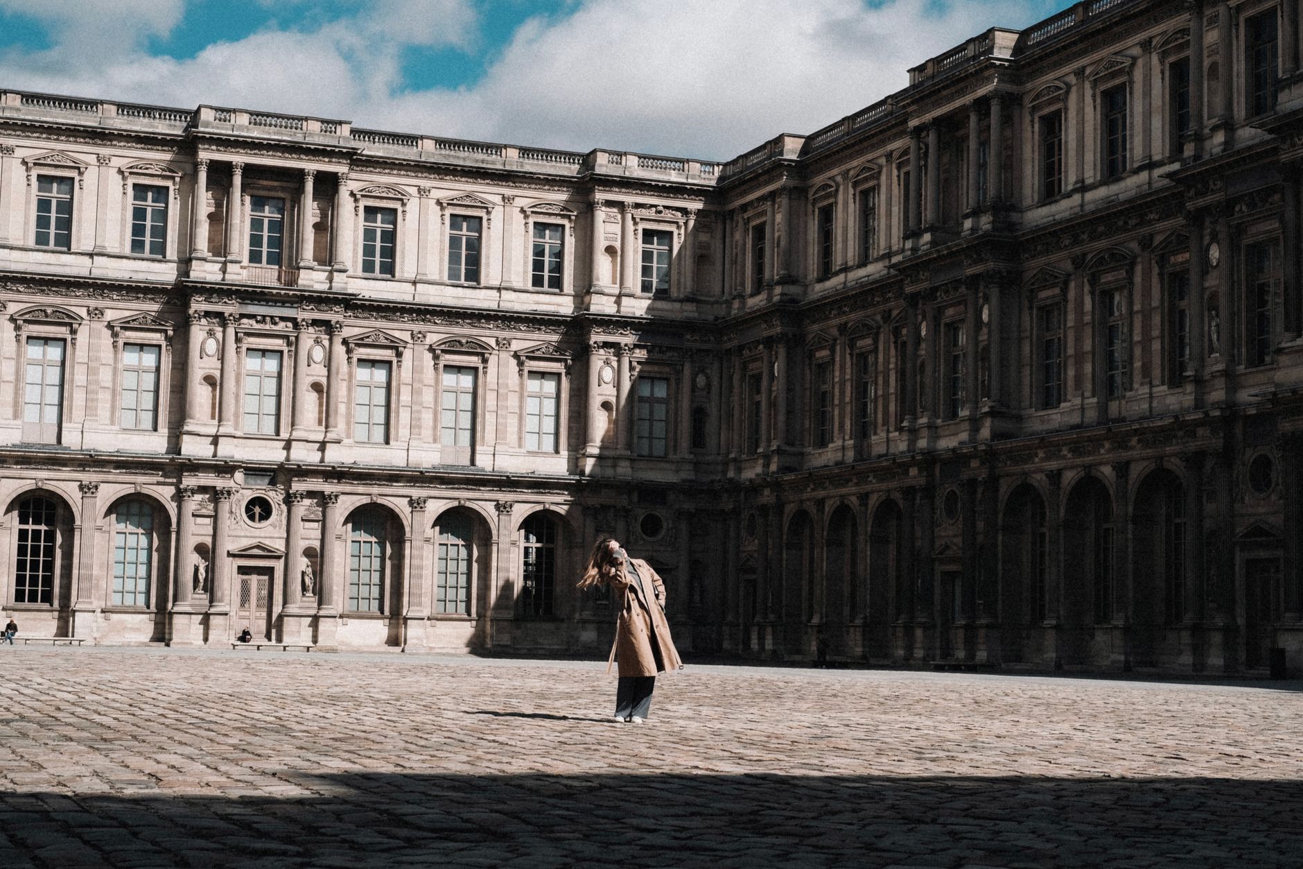 A woman in a stylish coat standing in the iconic Louvre courtyard, Paris.