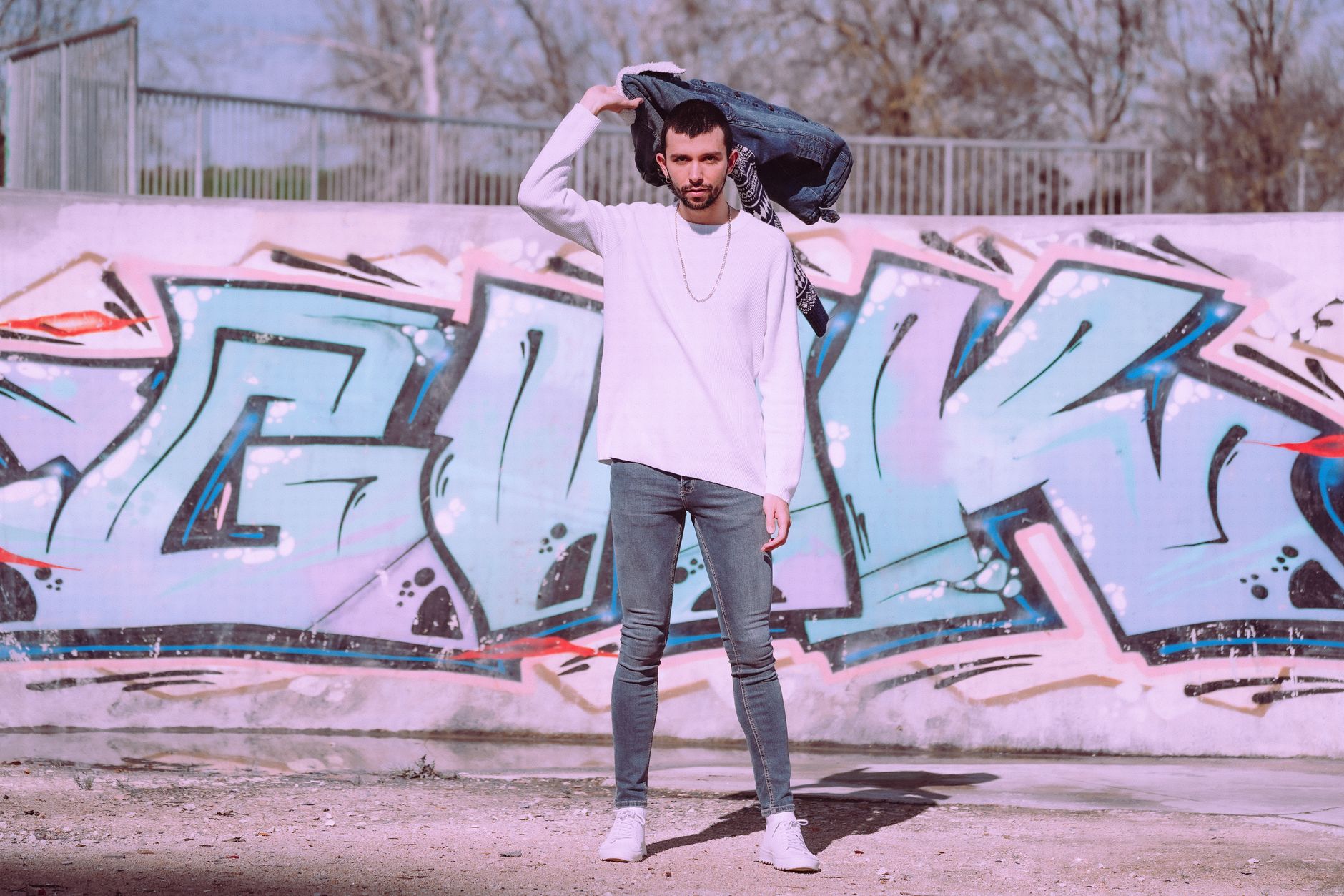 Stylish man poses in front of colorful graffiti wall outdoors, exuding modern urban style.