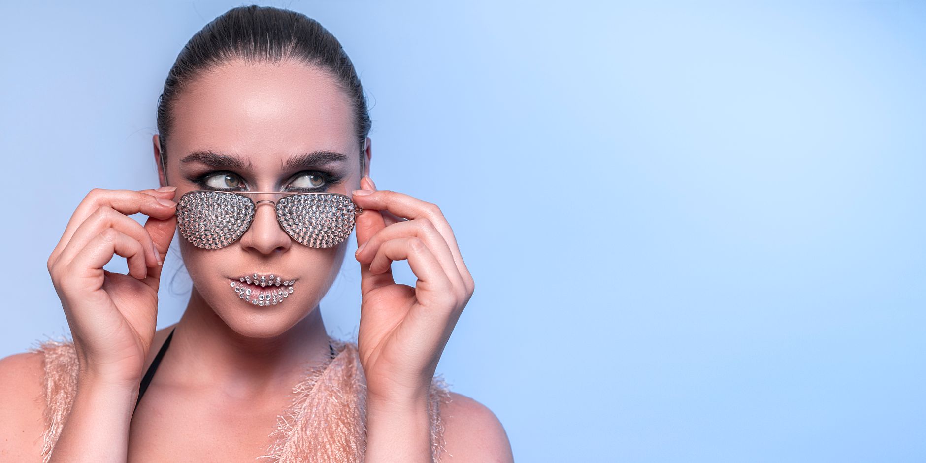 Elegant woman wearing rhinestone sunglasses with a blue backdrop, exuding a trendy and chic look.