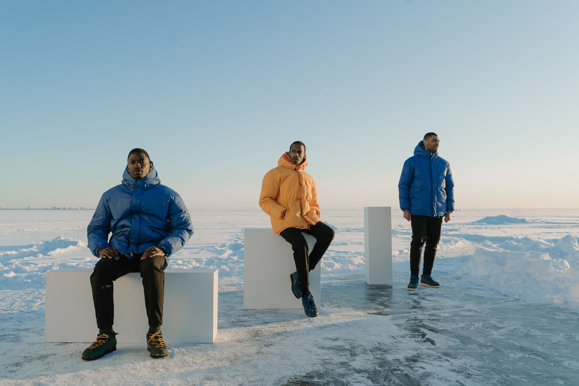 Three men in colorful puffer jackets pose on a snowy landscape with clear blue sky.