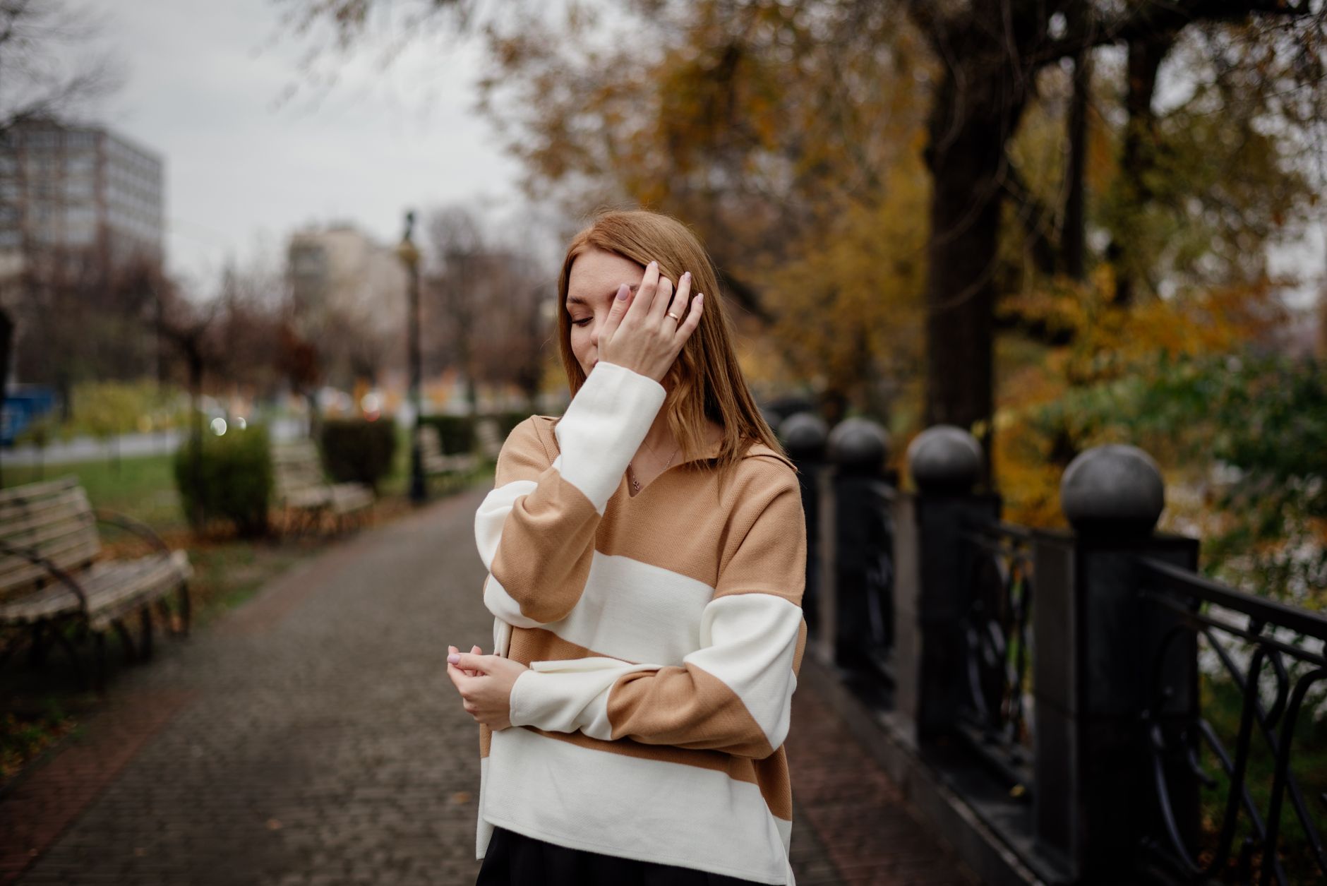 Woman in stylish sweater posing in urban park during autumn. Elegant and serene fall fashion portrait.
