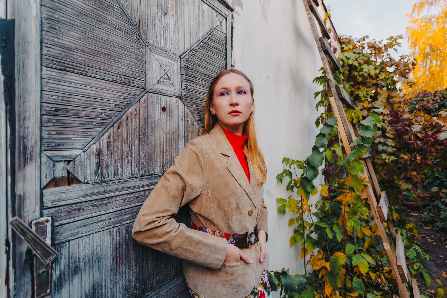 Stylish woman in suede jacket poses against vintage wooden door outdoors during fall.