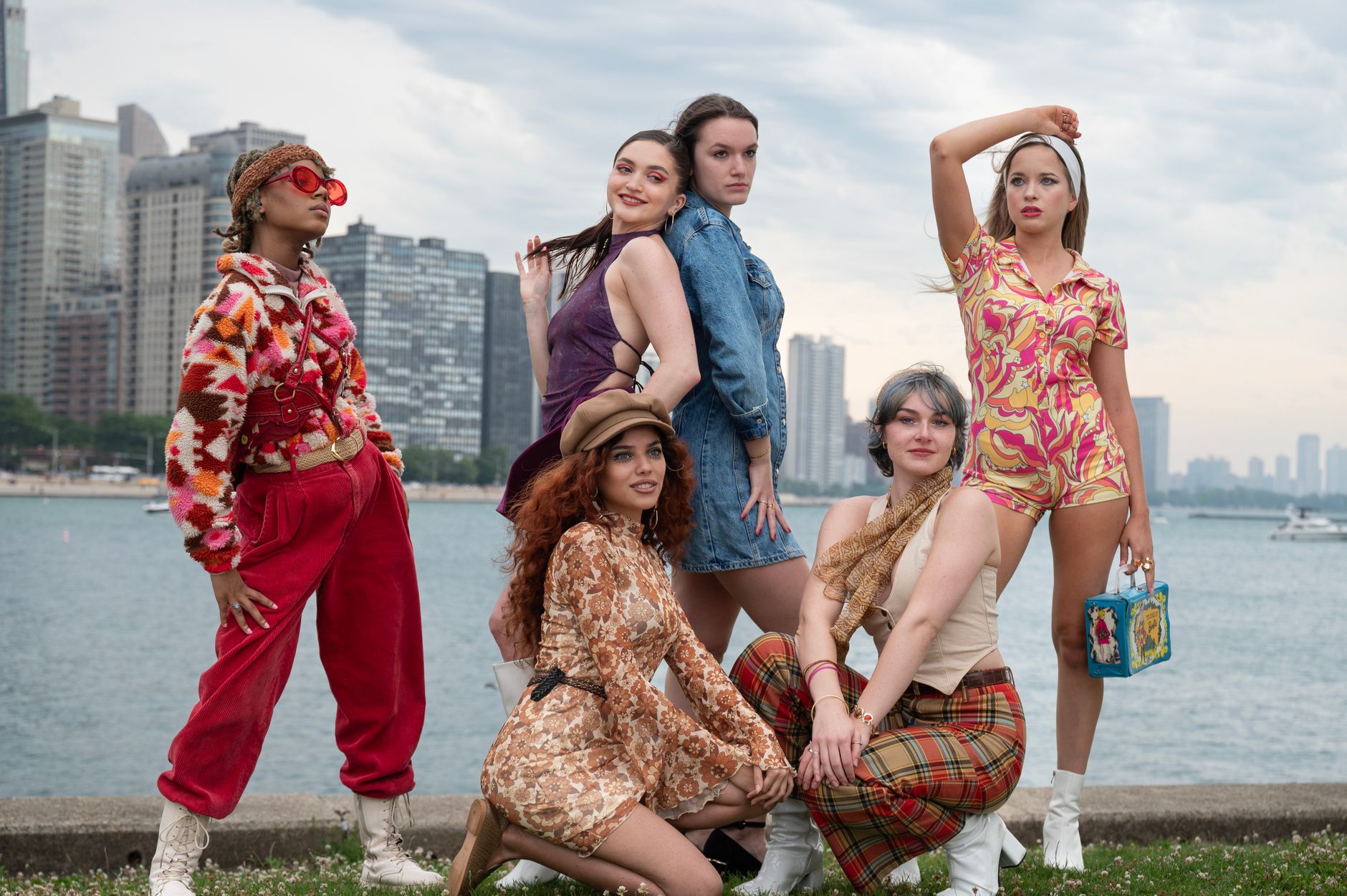 Young adults dressed in vintage fashion posing by a waterfront cityscape.