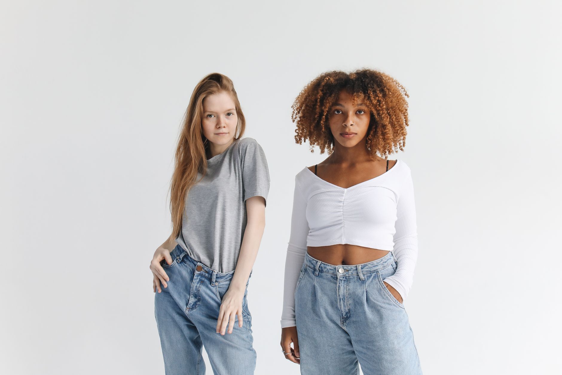 Two confident women posing in casual style with denim jeans and trendy tops.
