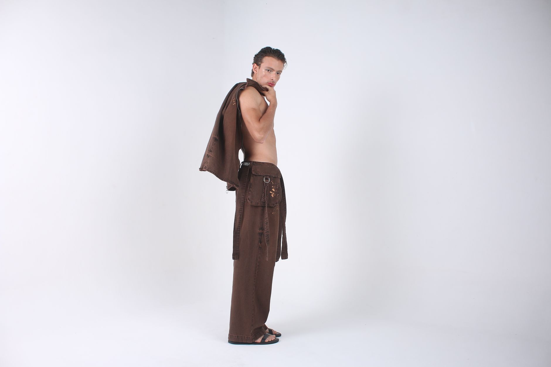 Fashion model striking a pose in elegant brown clothing against a white backdrop.
