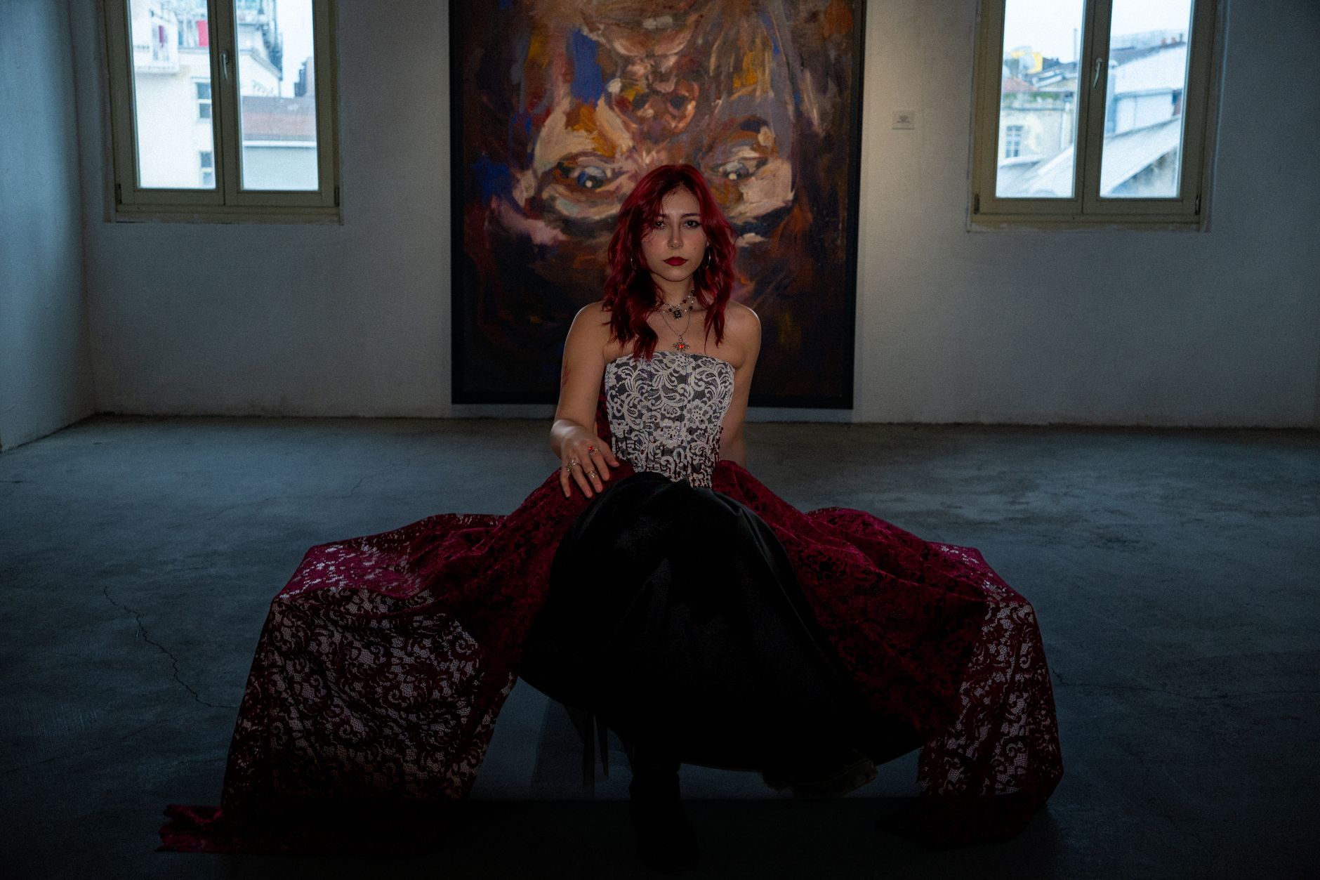 Woman in stylish dress sitting in art gallery with dramatic portrait backdrop.