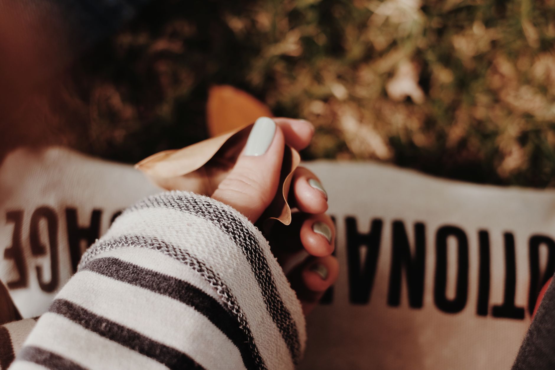 Close-up of a woman's manicured hand holding autumn leaves, conveying warmth and coziness.