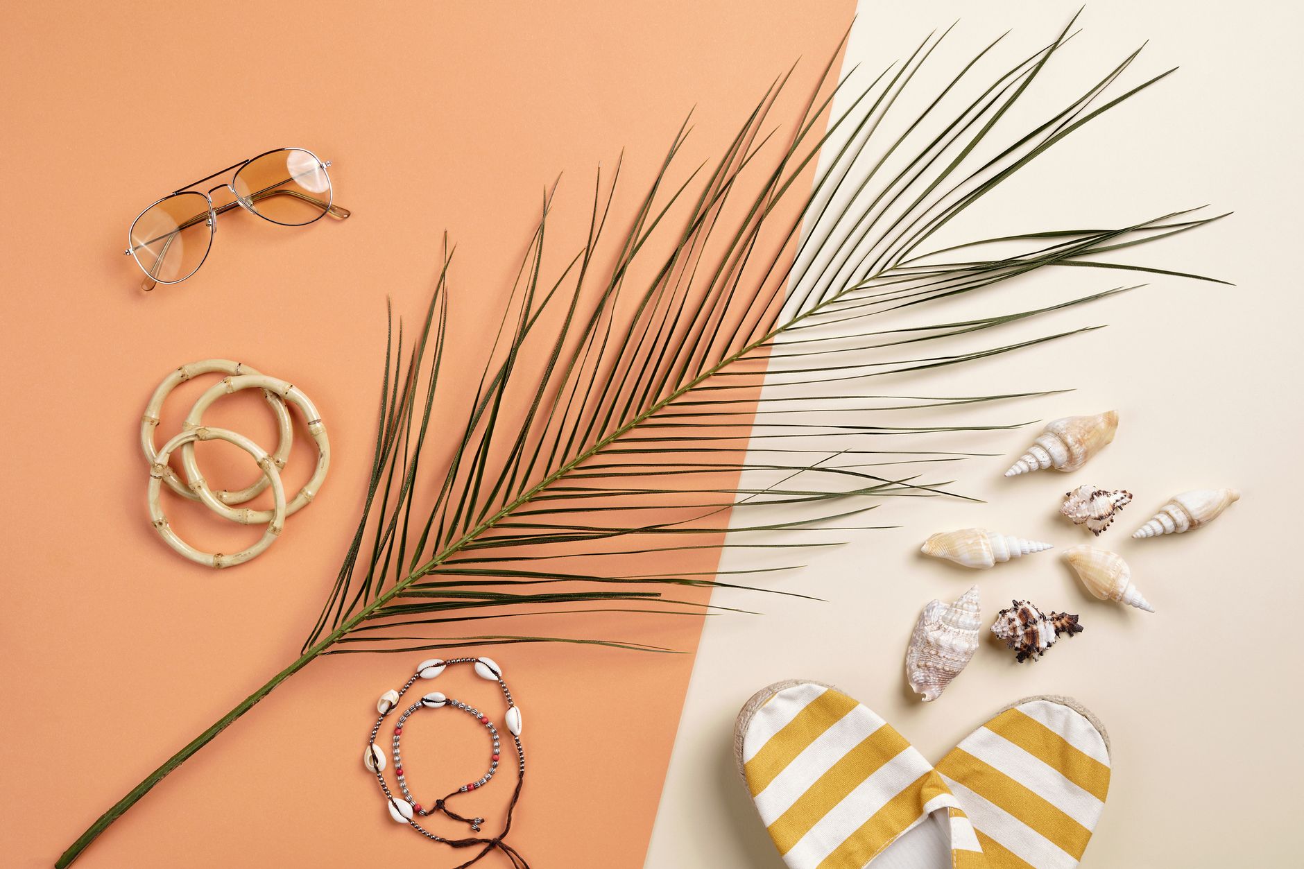 Colorful flat lay featuring summer accessories, seashells, and a palm leaf on a split background.