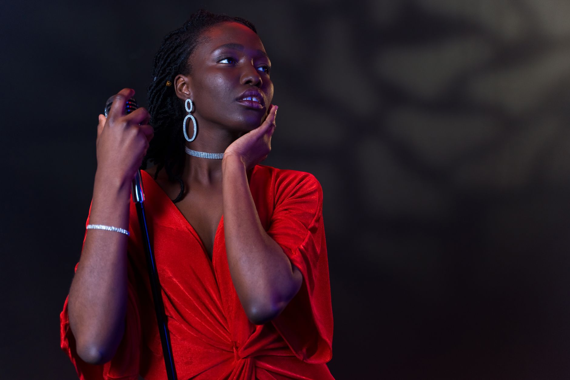 Elegant female vocalist in red dress holding a microphone, captured in dramatic lighting.