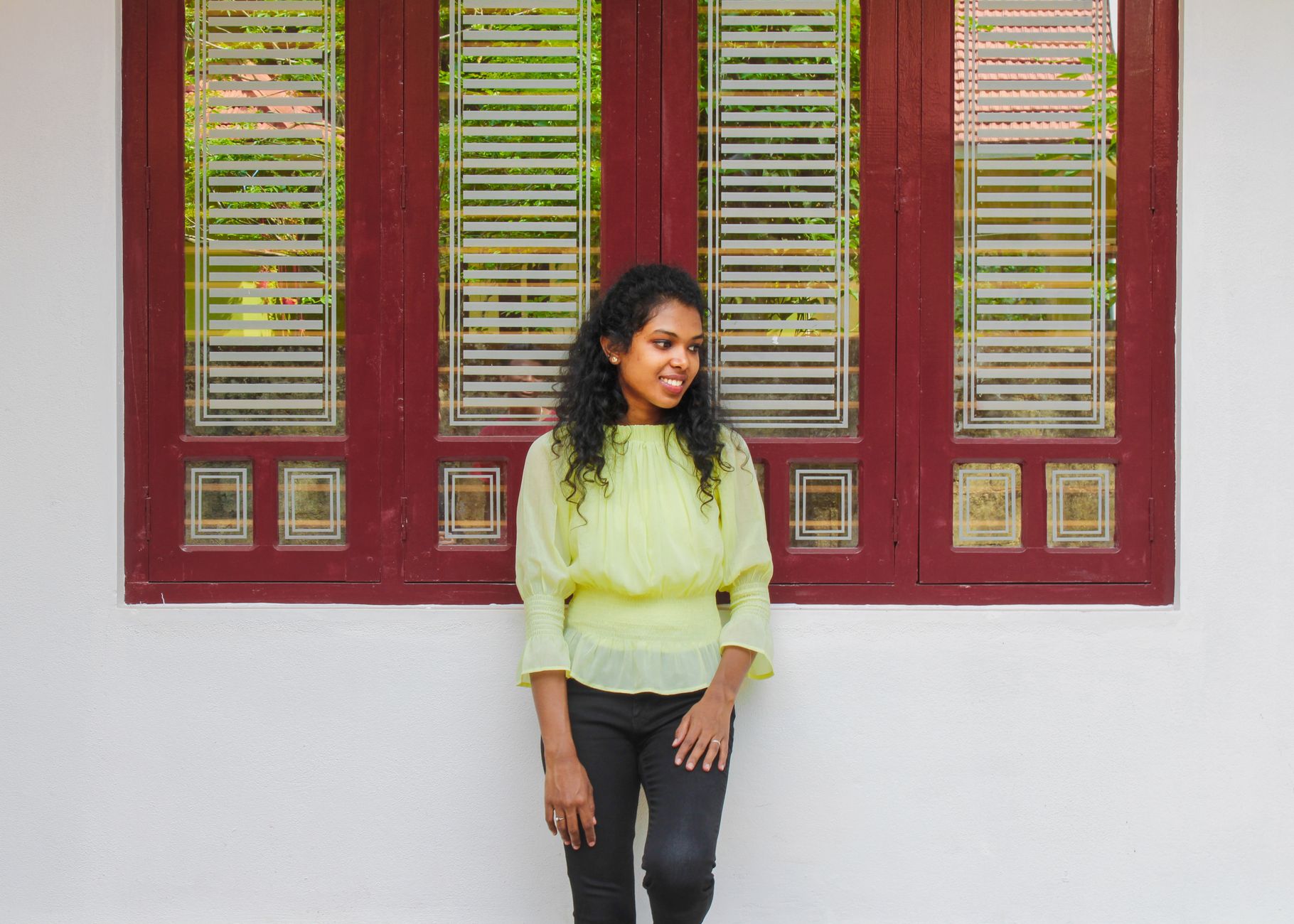 A woman standing in front of a red framed window, smiling in a lime green outfit.