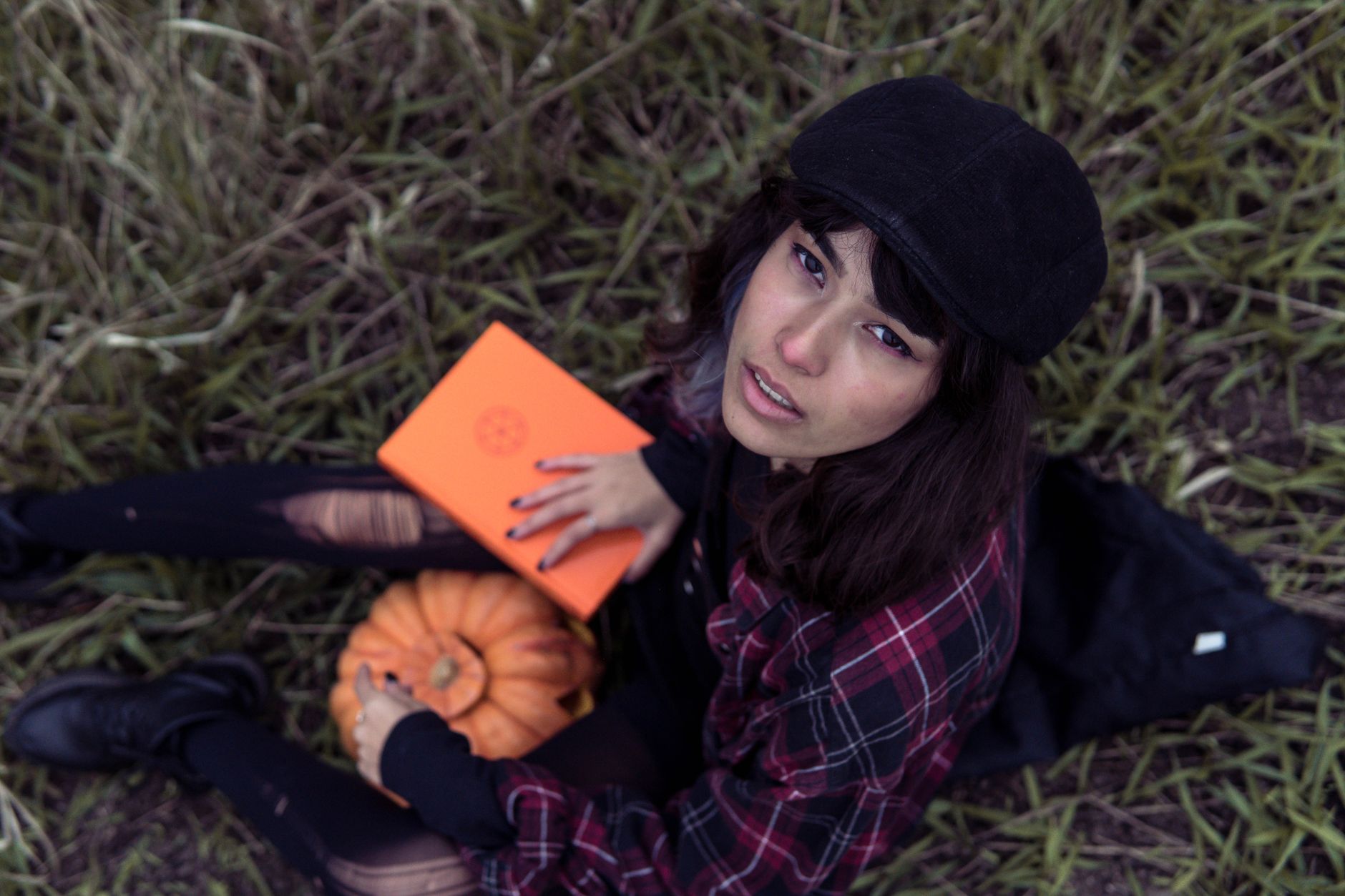 Fashionable woman sitting outdoors with a pumpkin, embodying autumn vibes.