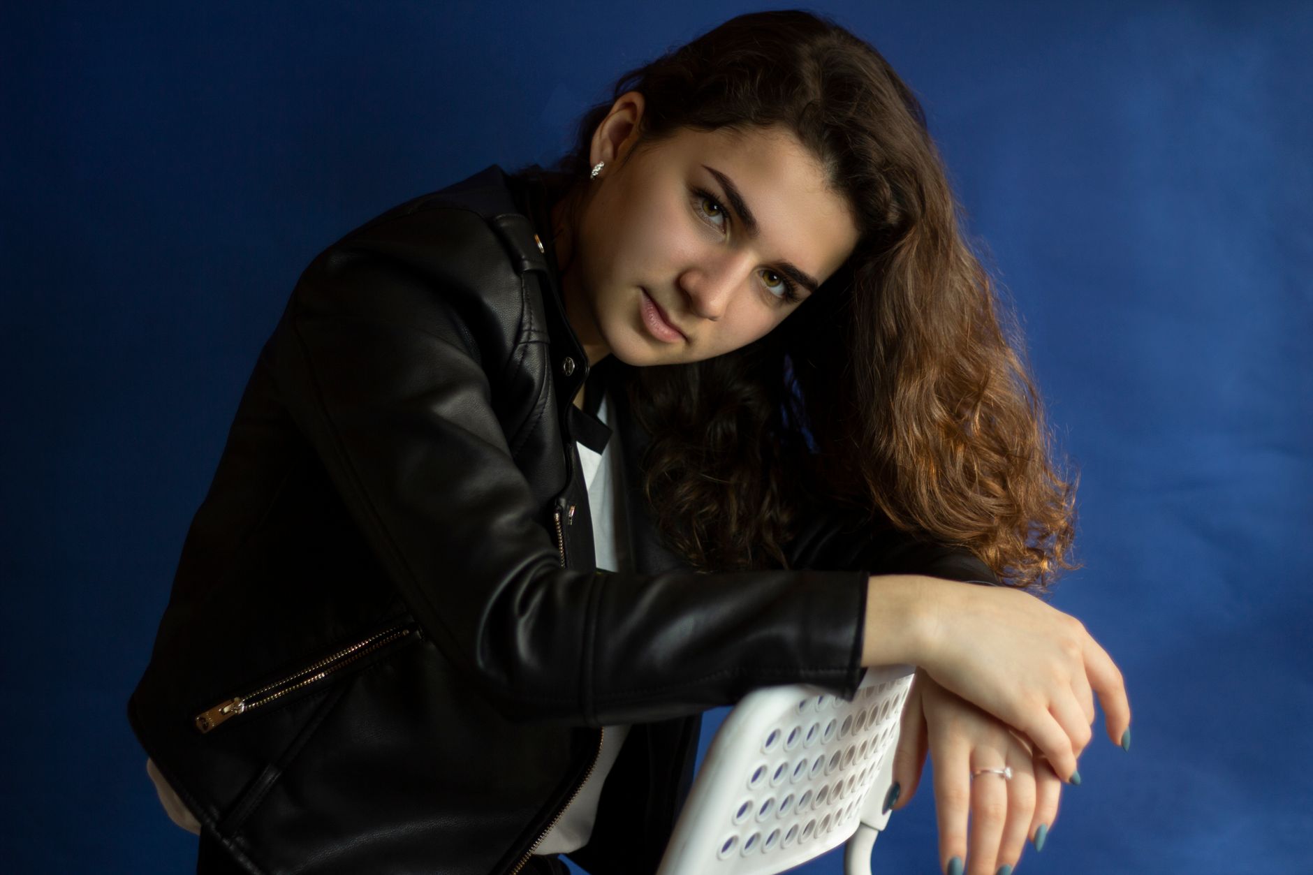 A captivating studio shot of a woman posing in a black leather jacket against a blue background.