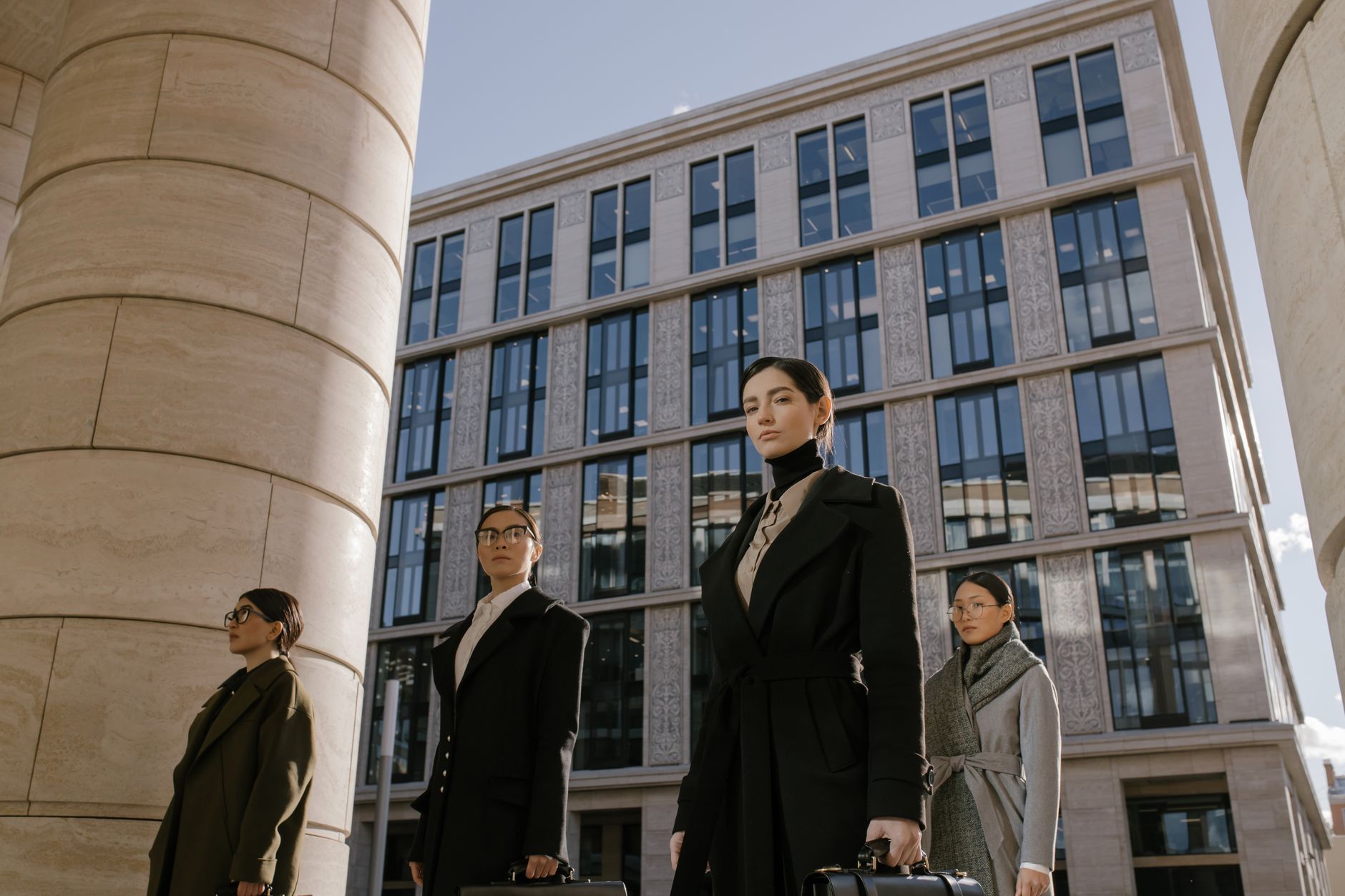 Elegant women in coats walking in a modern cityscape, embodying diversity and style.
