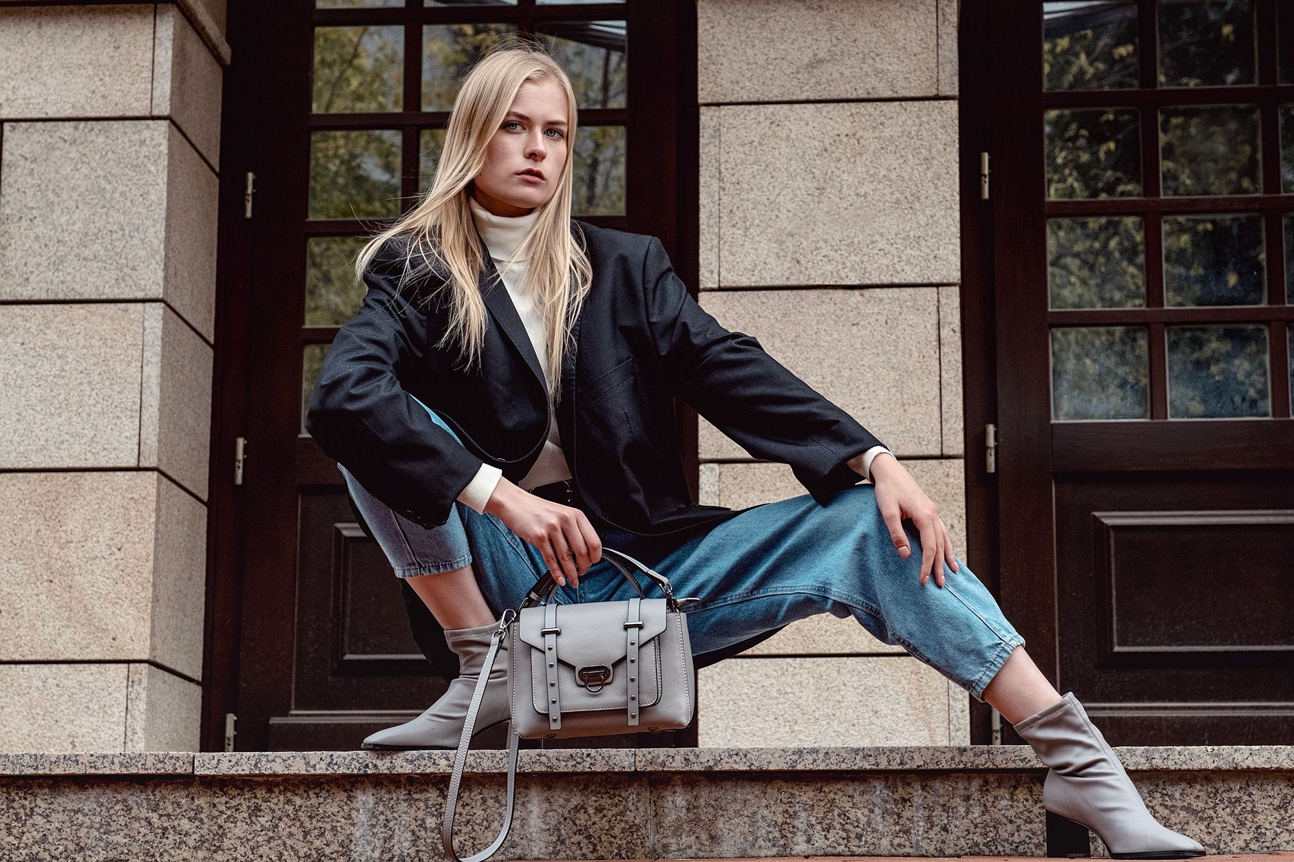Full length vogue young female in trendy outfit hunkering down confidently outside modern building and looking at camera