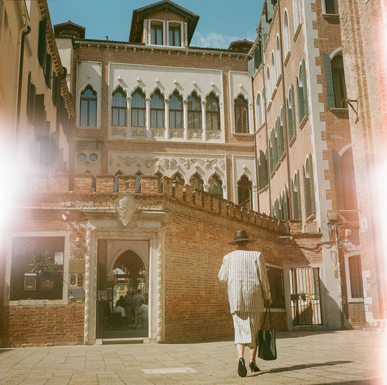 A stylish woman in striped outfit walks past a historic building in Venice, Italy, capturing the essence of Venetian architecture and fashio