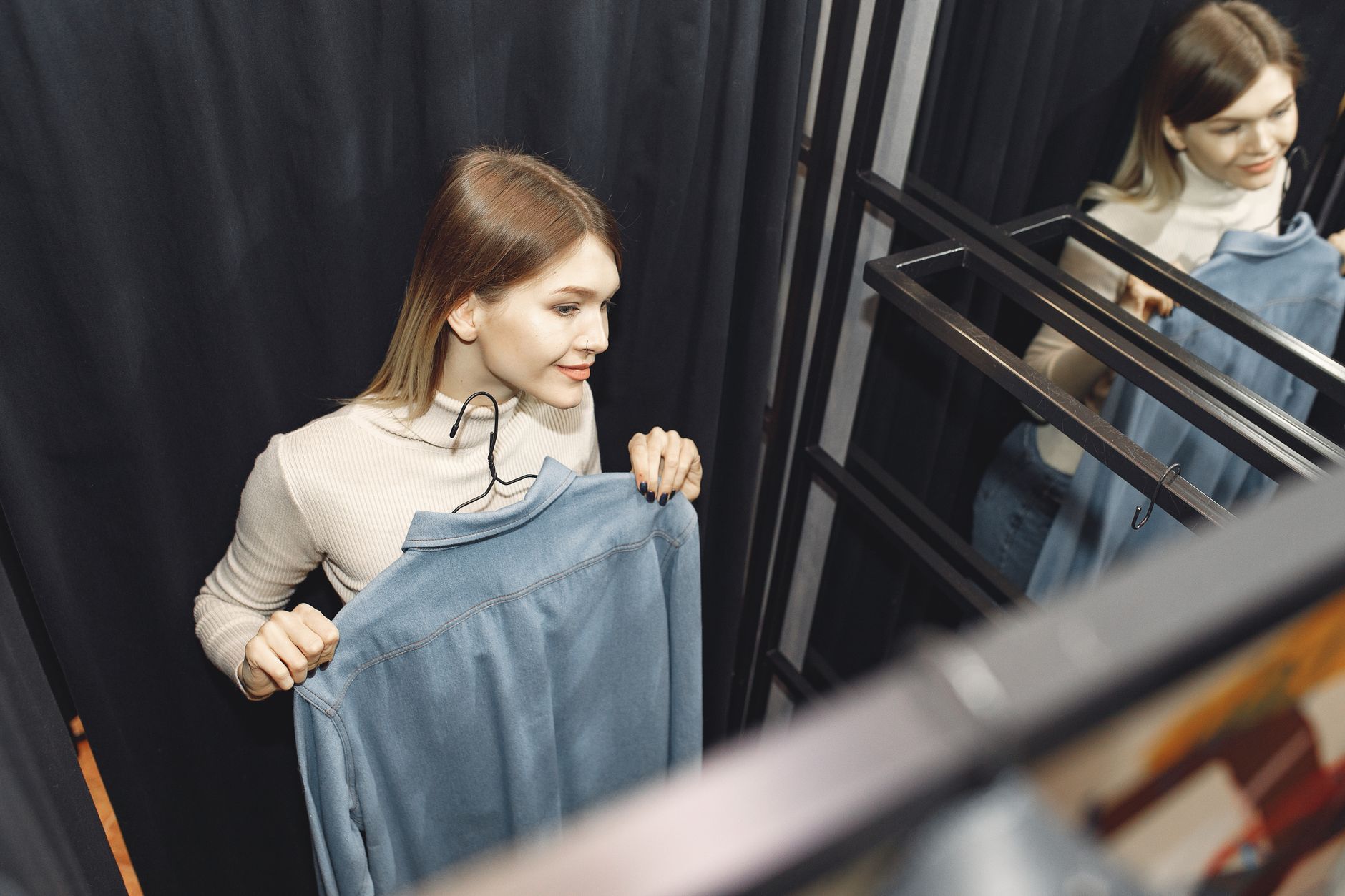 Young woman in fitting room holding clothes near a mirror.