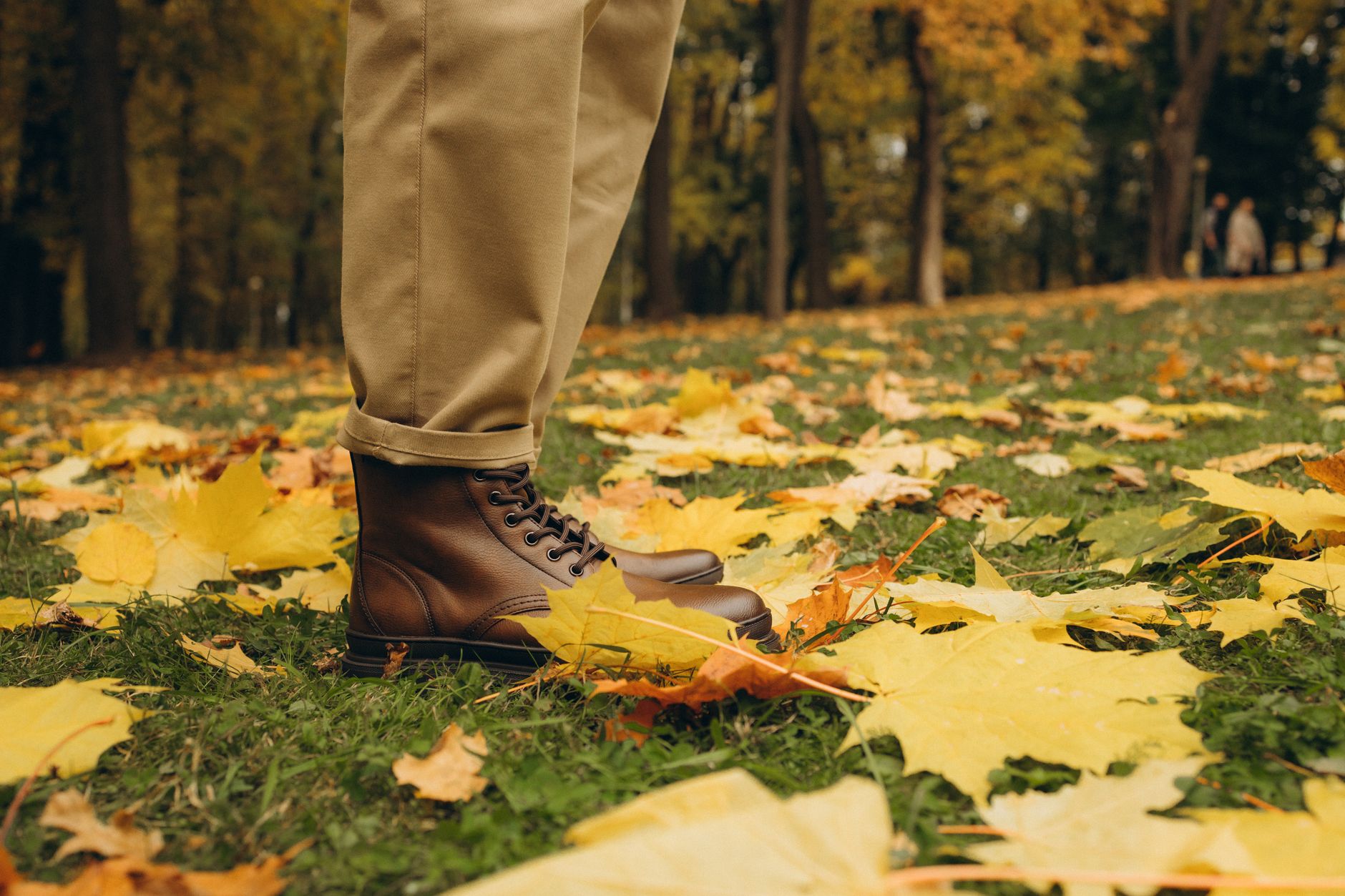 Close-up of brown leather boots standing on vibrant autumn leaves in a park.