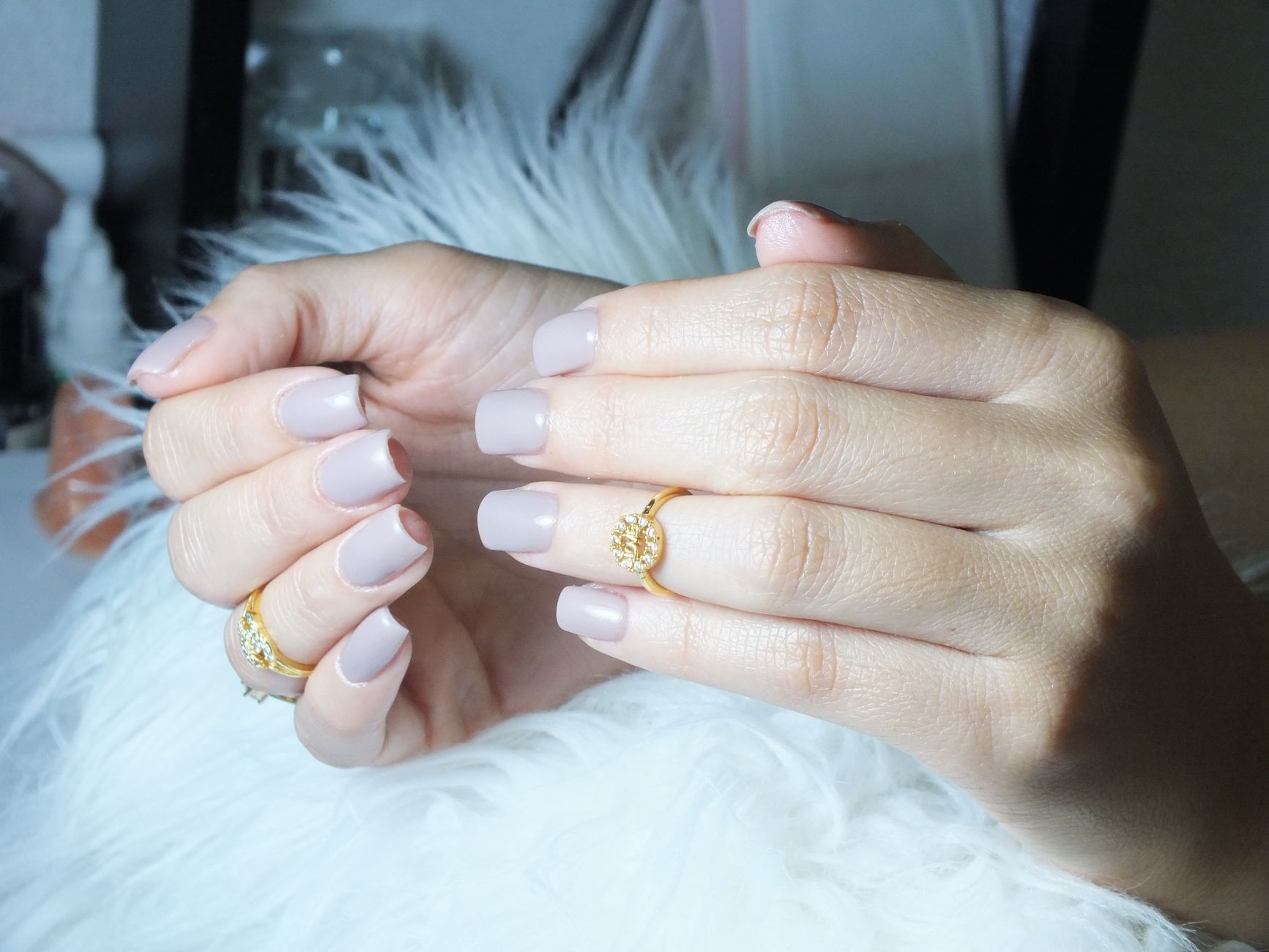 Close-up of beautiful manicured hands showcasing grey nails and gold rings in a serene setting.